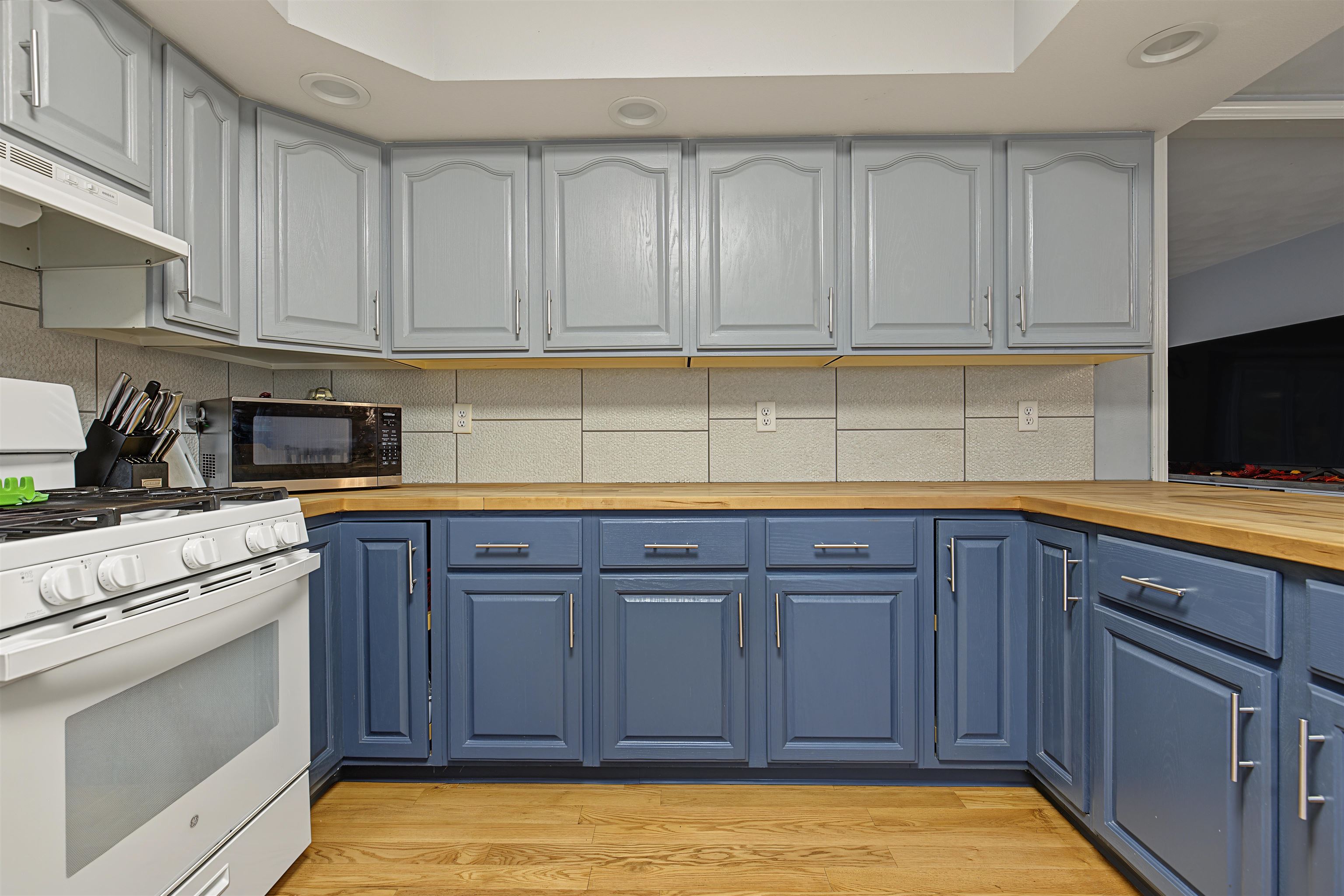 Kitchen with blue lower cabinets, gray upper cabinets, wood countertops, and a white range.