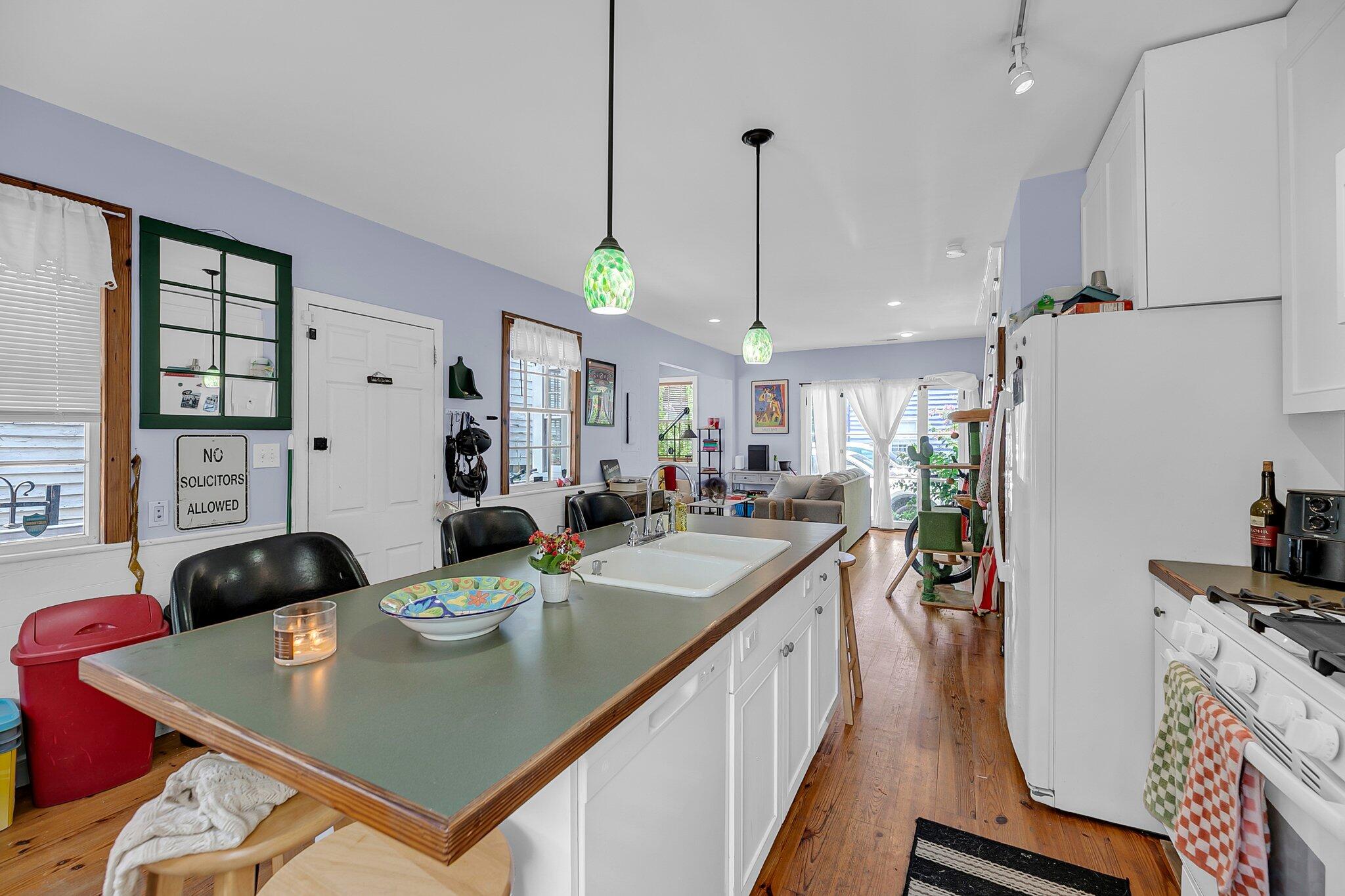 Kitchen with a long green island, pendant lights, white cabinetry, and an adjoining living area.