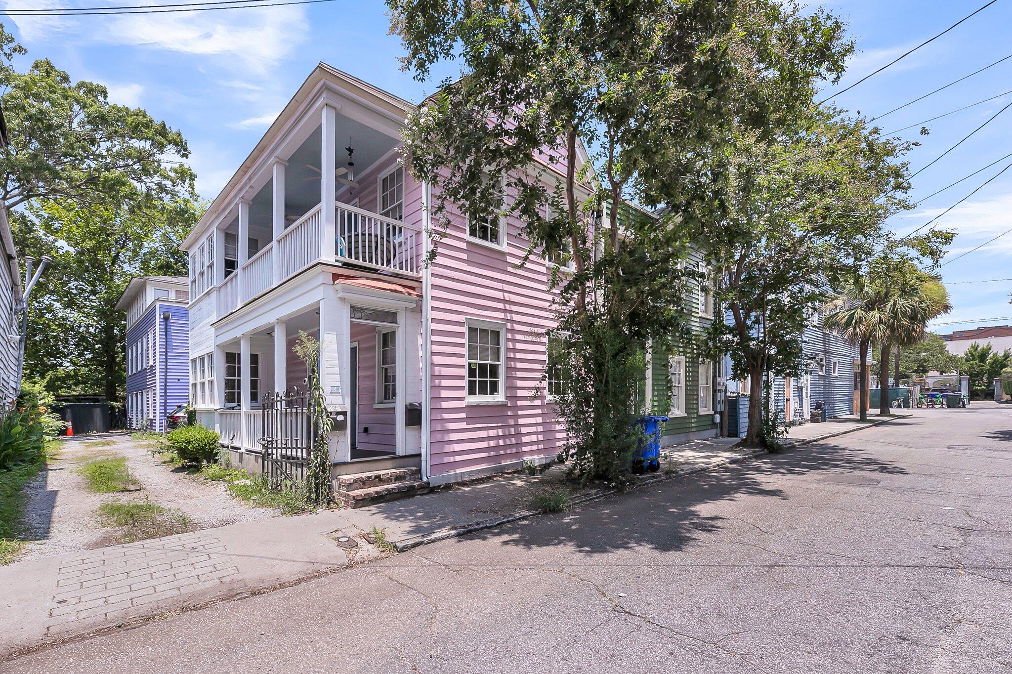 Two-story pink house with white trim, a covered porch, and an upper balcony.