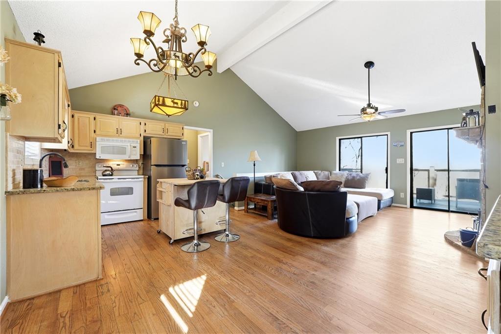 Open kitchen and living room with vaulted ceiling, hardwood floors, and sliding doors overlooking the water.