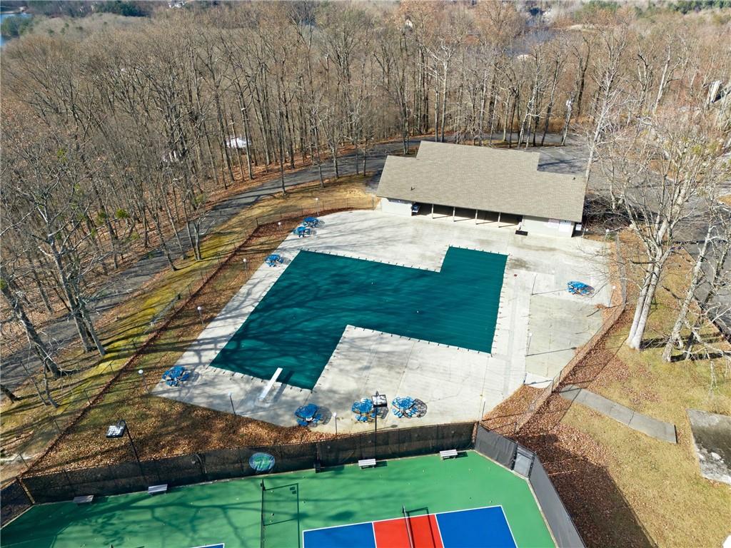 Aerial view of a covered pool, pavilion, and colorful court among leafless trees.