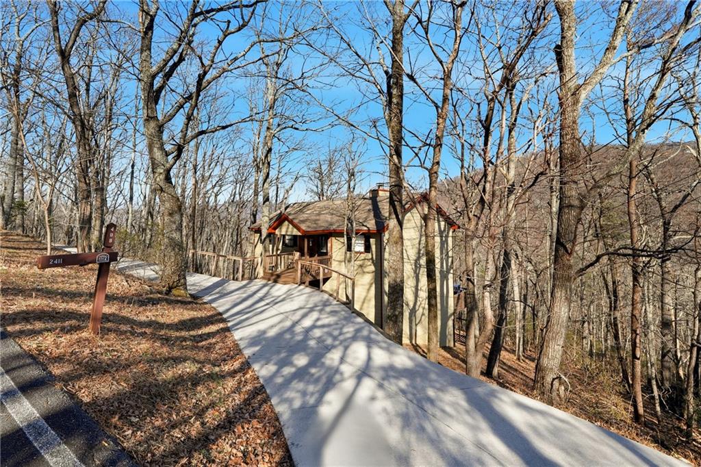 Tan house with red trim at the end of a driveway among leafless trees.