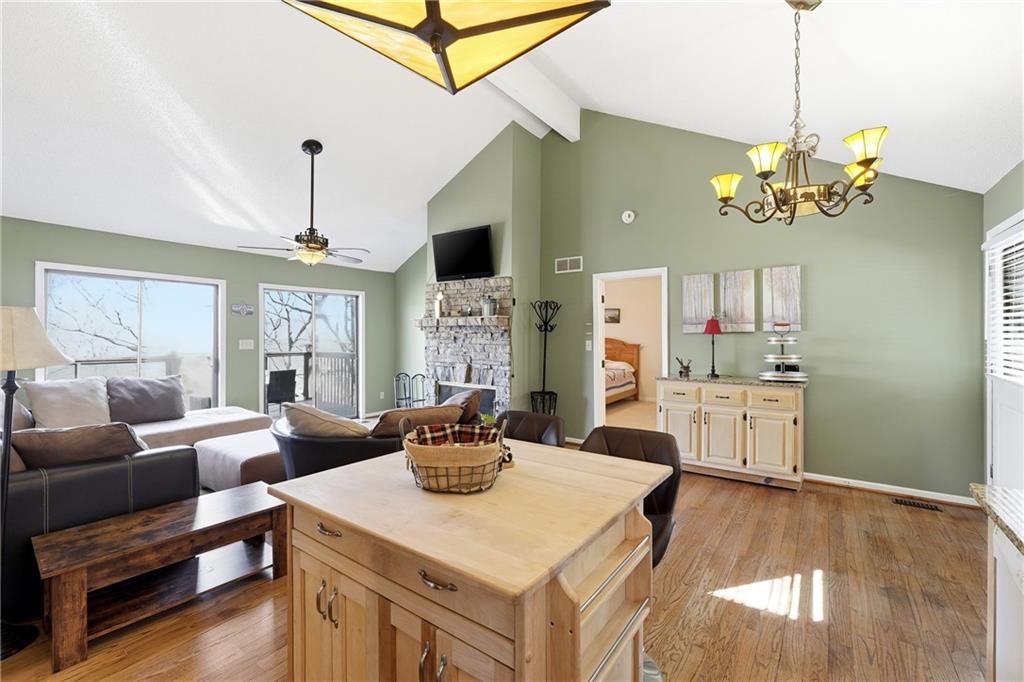 Open living and dining area with a wood island, stone fireplace, and deck access.