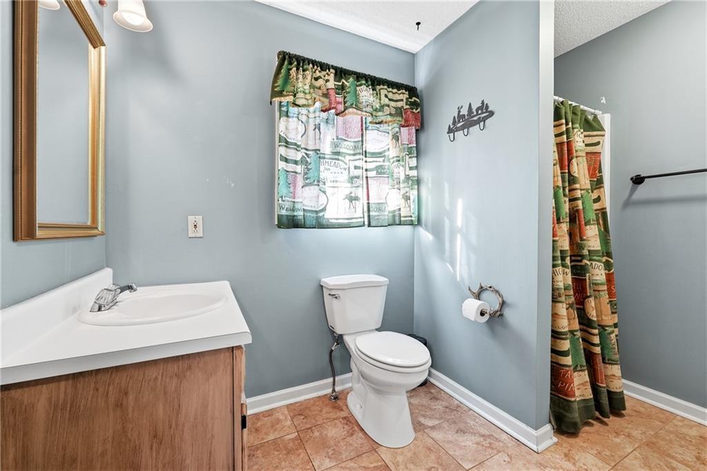 Bathroom with a wood vanity, white toilet, patterned shower curtain, and tan tile floor.