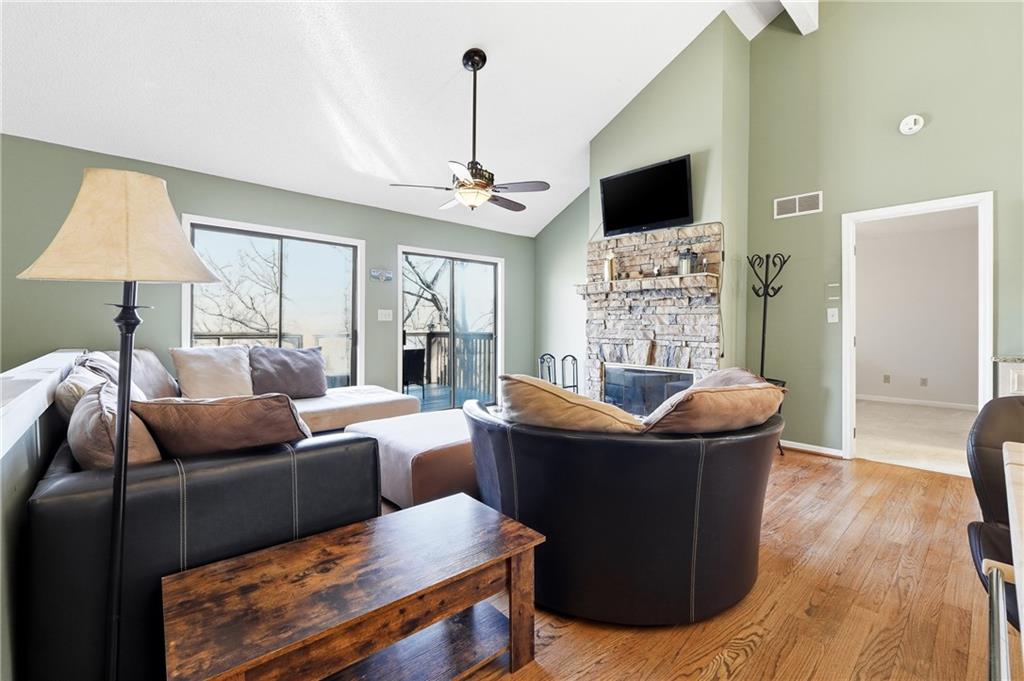 Furnished living room with a stone fireplace, vaulted ceiling, and glass doors to a deck.