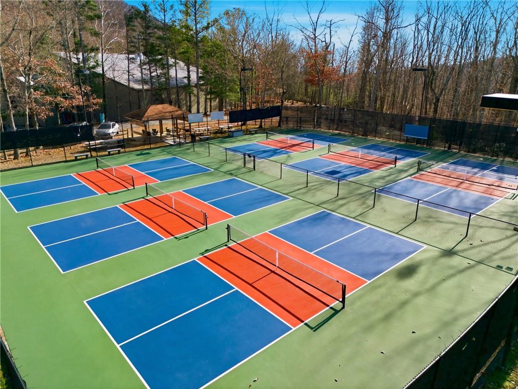 Multiple blue and orange pickleball courts with nets and fencing, surrounded by leafless trees.