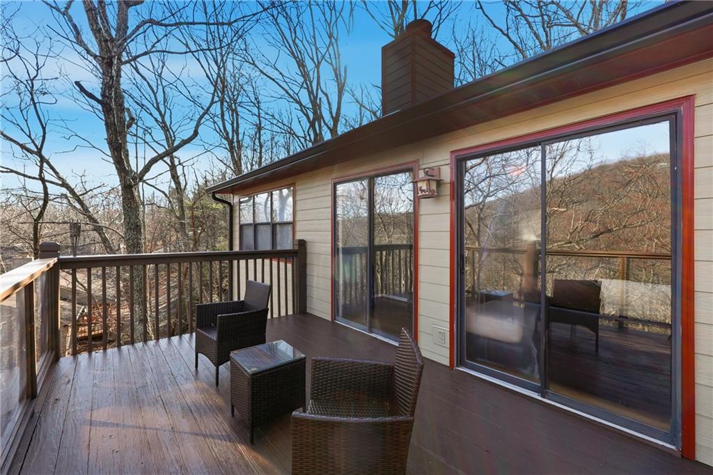 Wooden deck with wicker seating beside sliding glass doors, overlooking leafless trees.