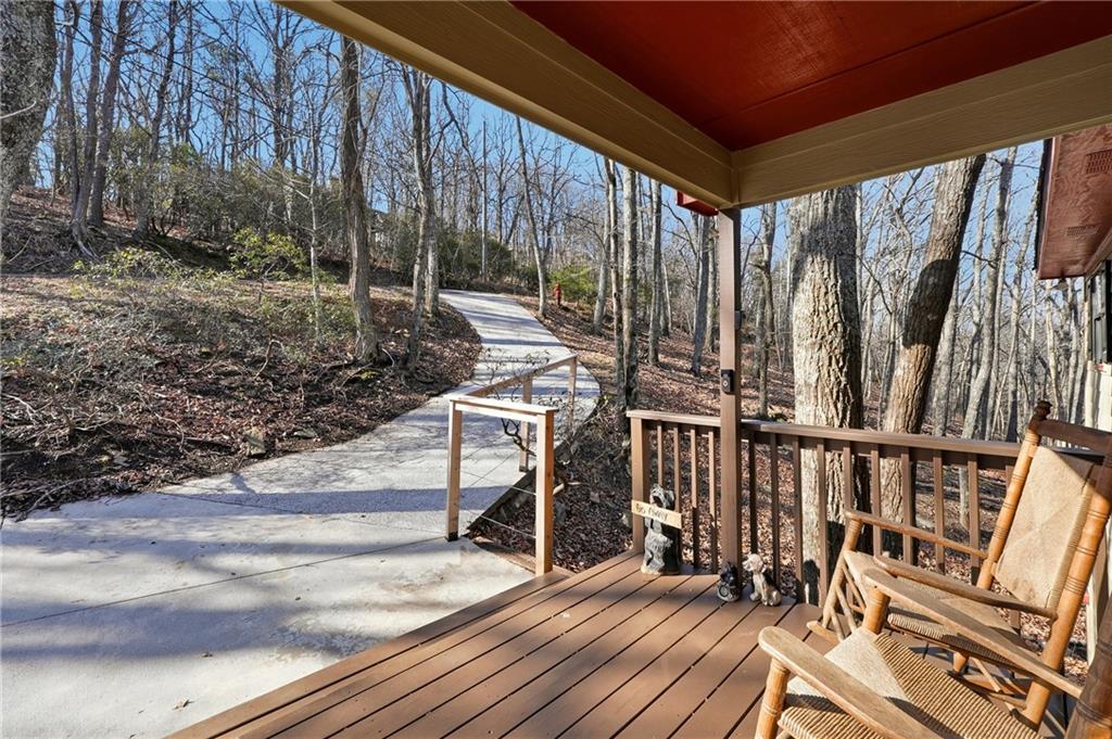 Covered porch with rocking chairs overlooking a winding walkway through leafless woods.