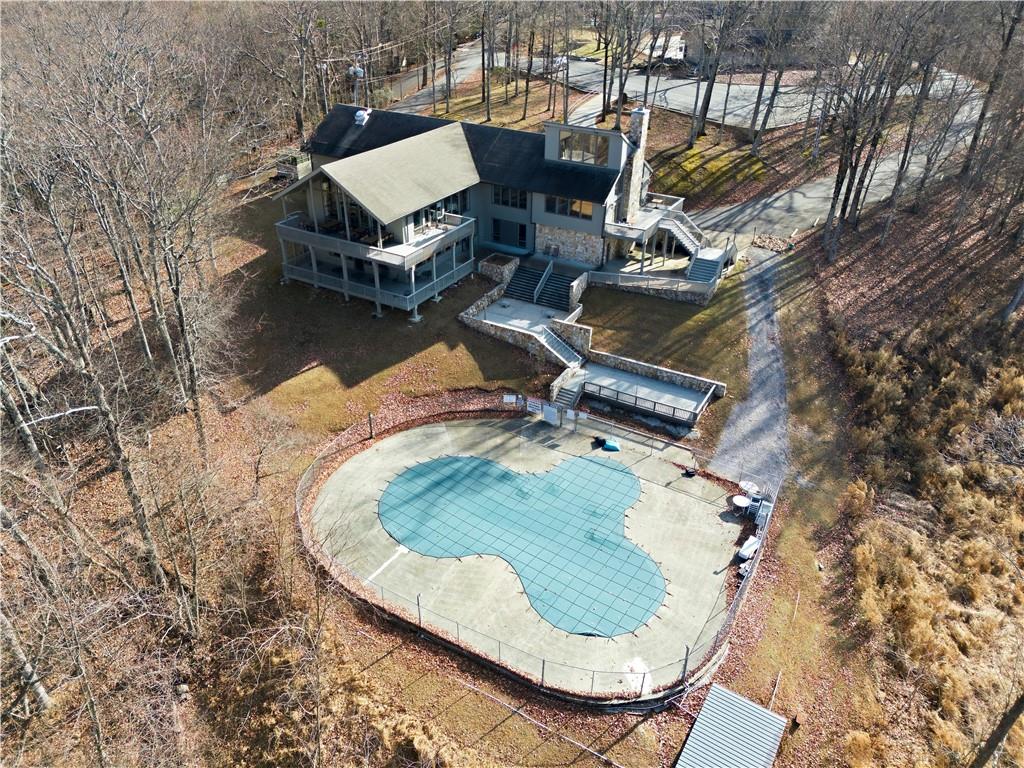 Aerial view of a wooded home with a kidney-shaped pool and broad paved deck.