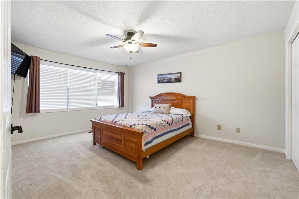 Bedroom with a wooden bed, patterned quilt, ceiling fan, and wide window with blinds.