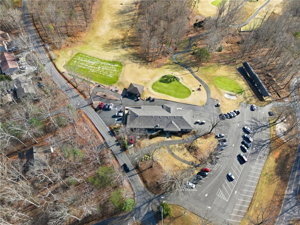 Aerial view of a building with a large parking lot, curved paths, and wooded grounds.