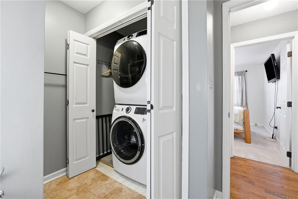 Laundry closet with stacked front-loading washer and dryer, open doors, and tiled floor.
