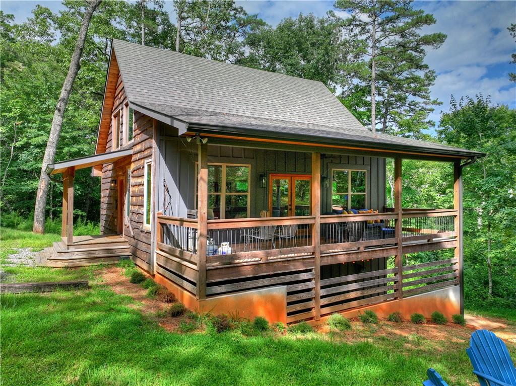 Wood-sided cabin with a spacious covered porch and deck surrounded by trees.