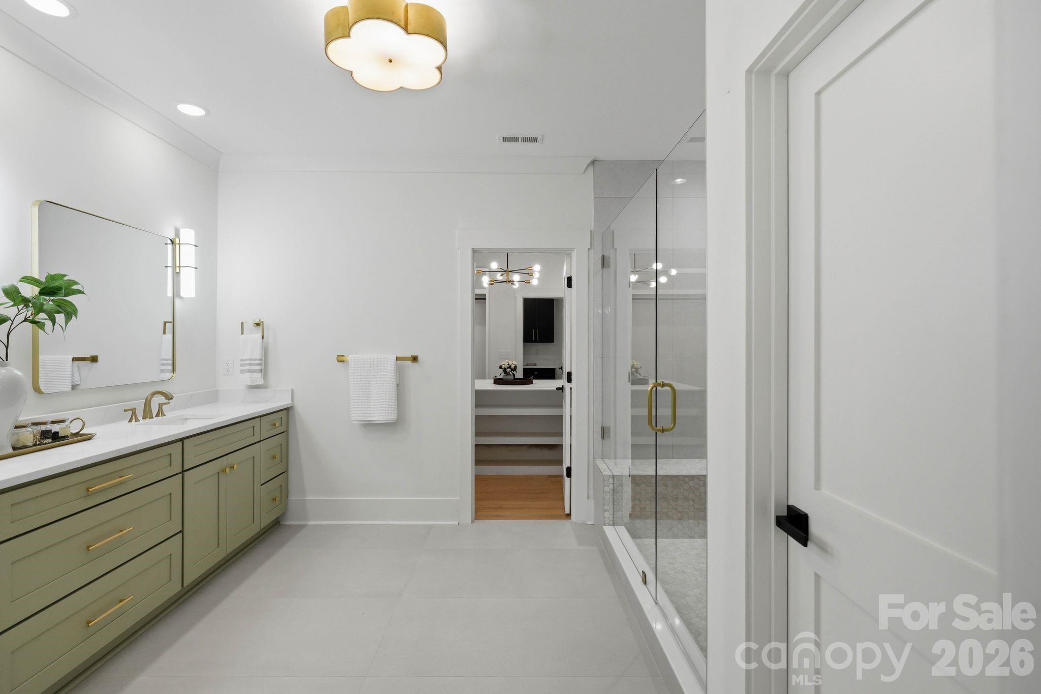 Modern bathroom with sage-green vanity, brass fixtures, large mirror, and glass-enclosed shower.