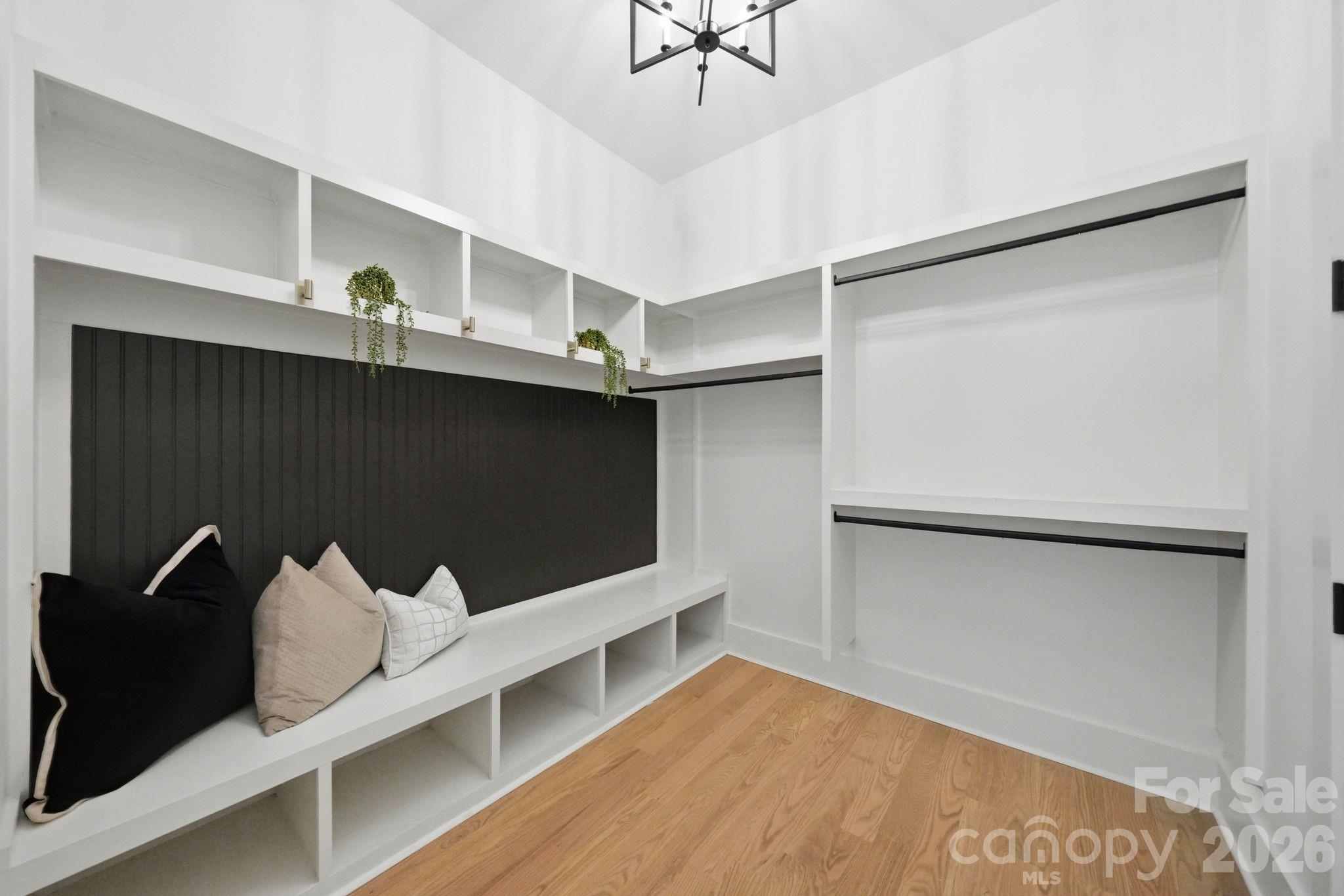 Walk-in closet with white built-ins, black accent wall, cushioned bench, and warm wood flooring.