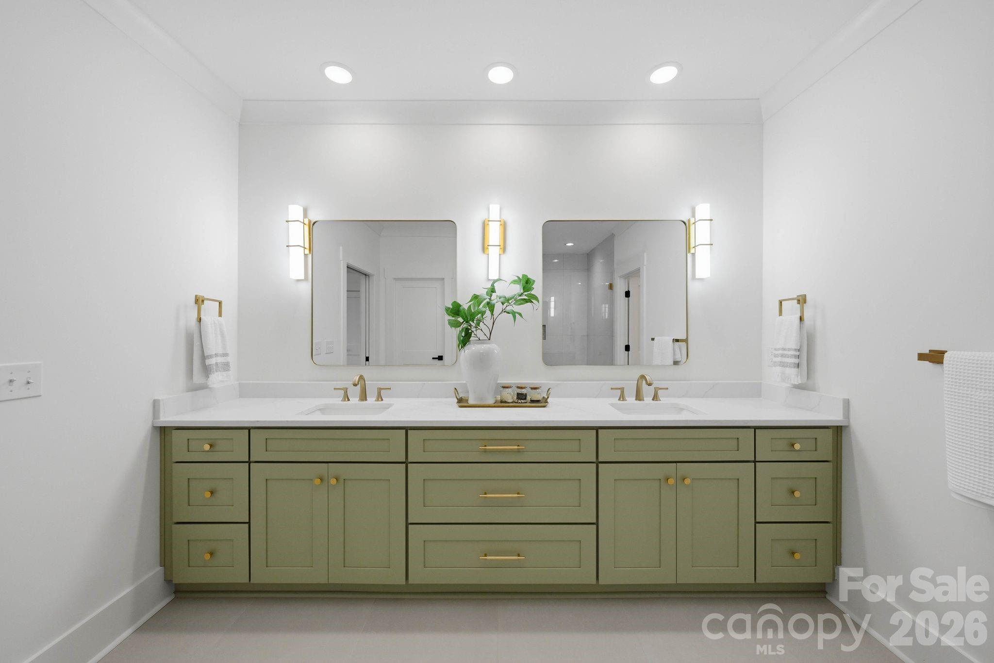 Bathroom with a sage-green double vanity, two sinks, gold fixtures, and matching framed mirrors.