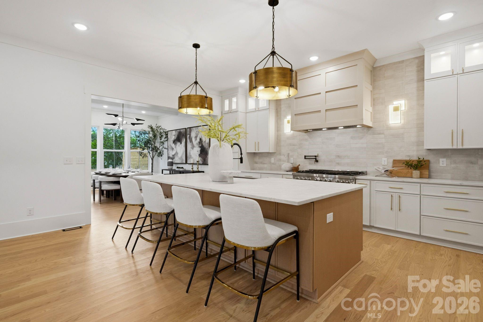 Modern kitchen with a large island, upholstered bar stools, brass pendants, and an adjoining dining area.