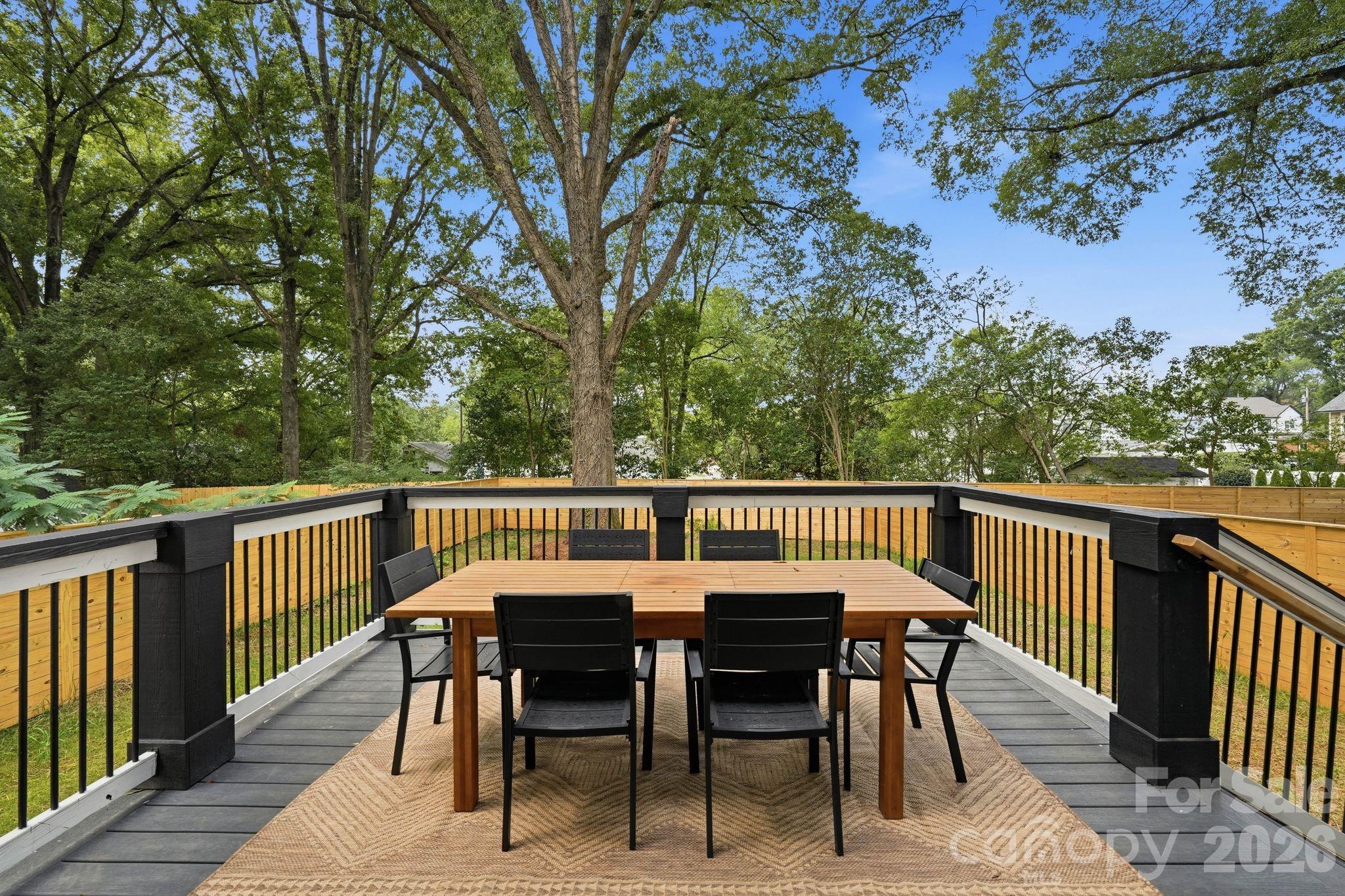 Outdoor deck with dining table and chairs, black railings, and a leafy fenced yard.