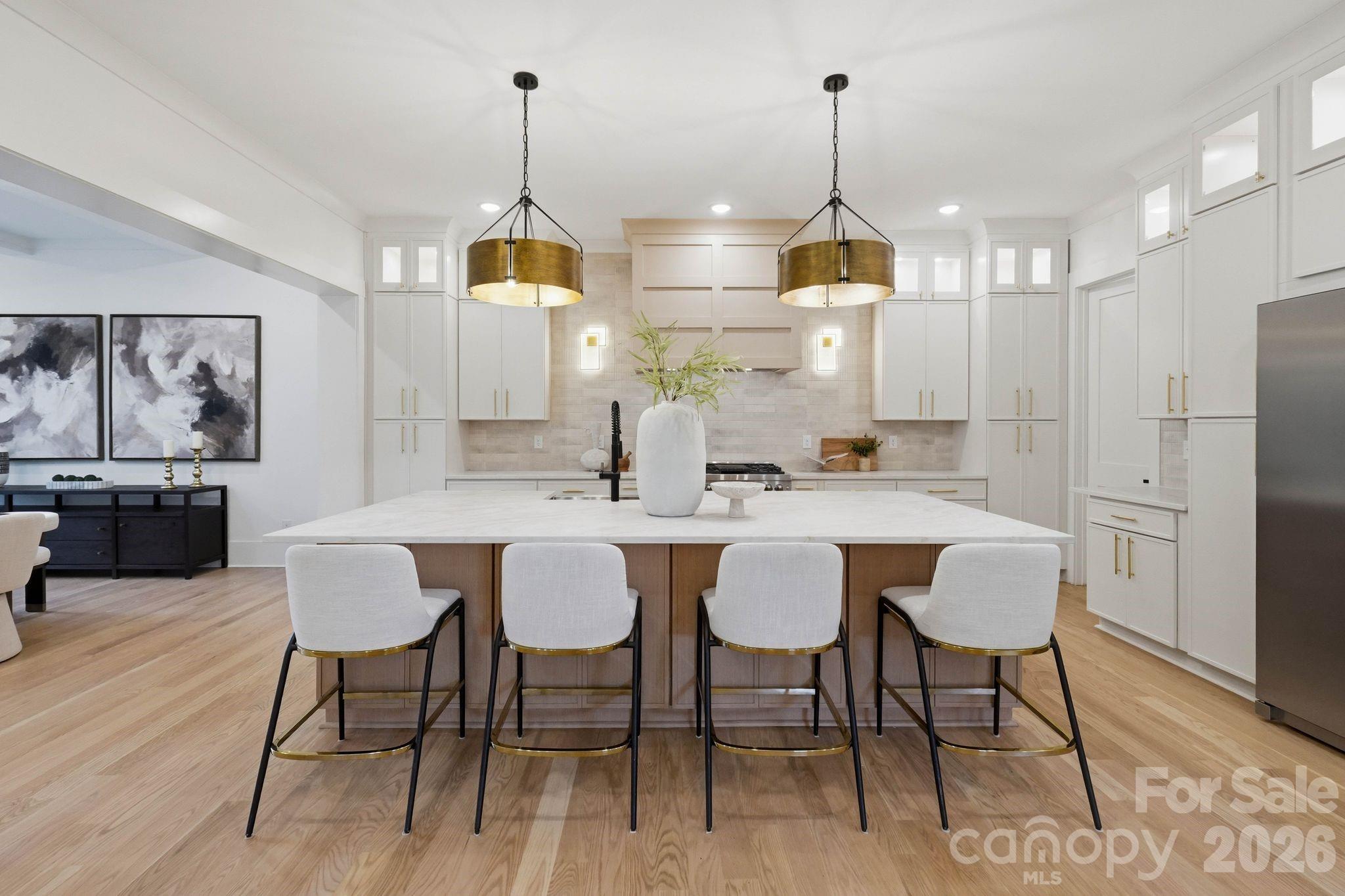 Kitchen with a large island, four bar stools, white cabinetry, and brass pendant lights.
