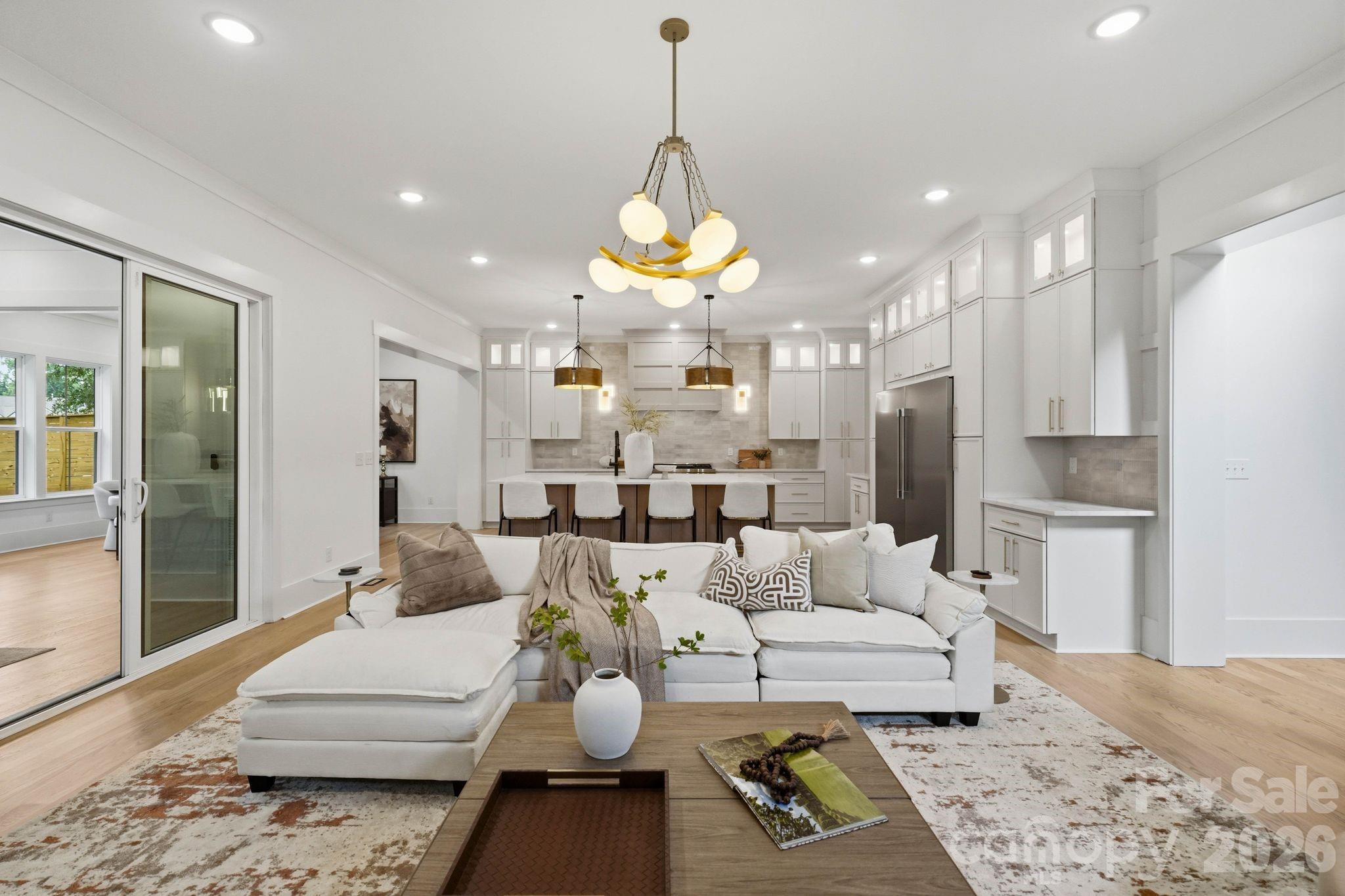 Open-plan living room and kitchen with a white sectional, extensive white cabinetry, and gold pendant lights.