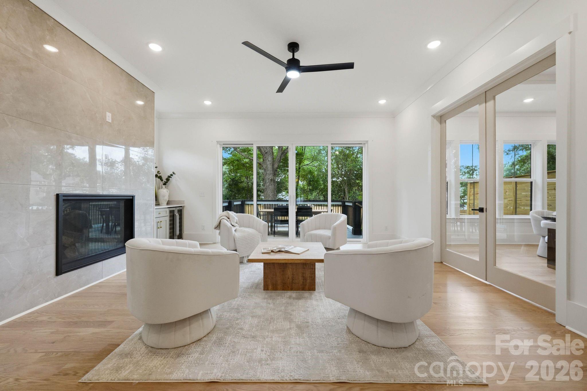 Furnished living room with tiled fireplace and glass doors opening to a tree-lined deck.