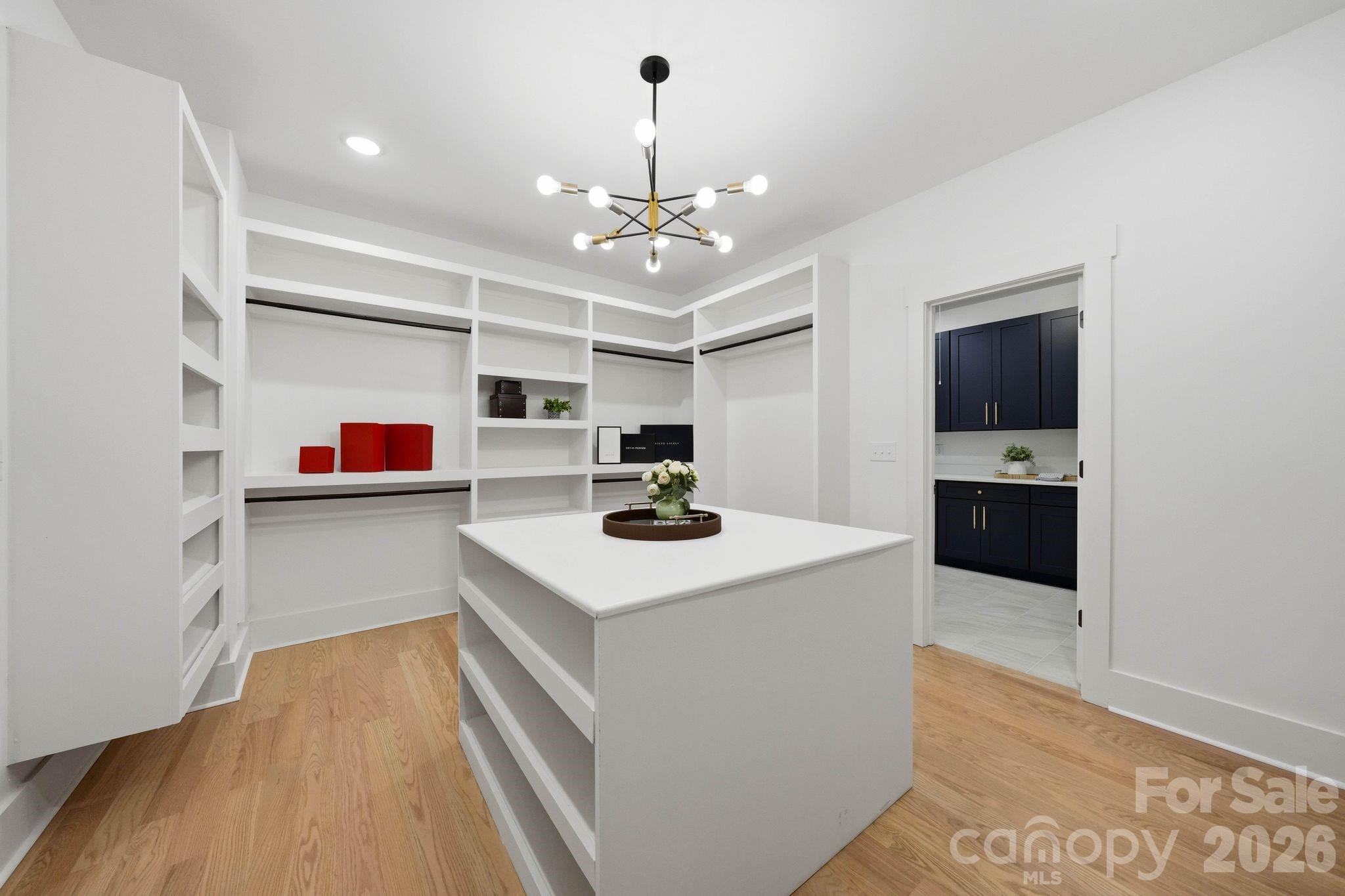 Walk-in closet with white built-ins, a central island, and light wood flooring.