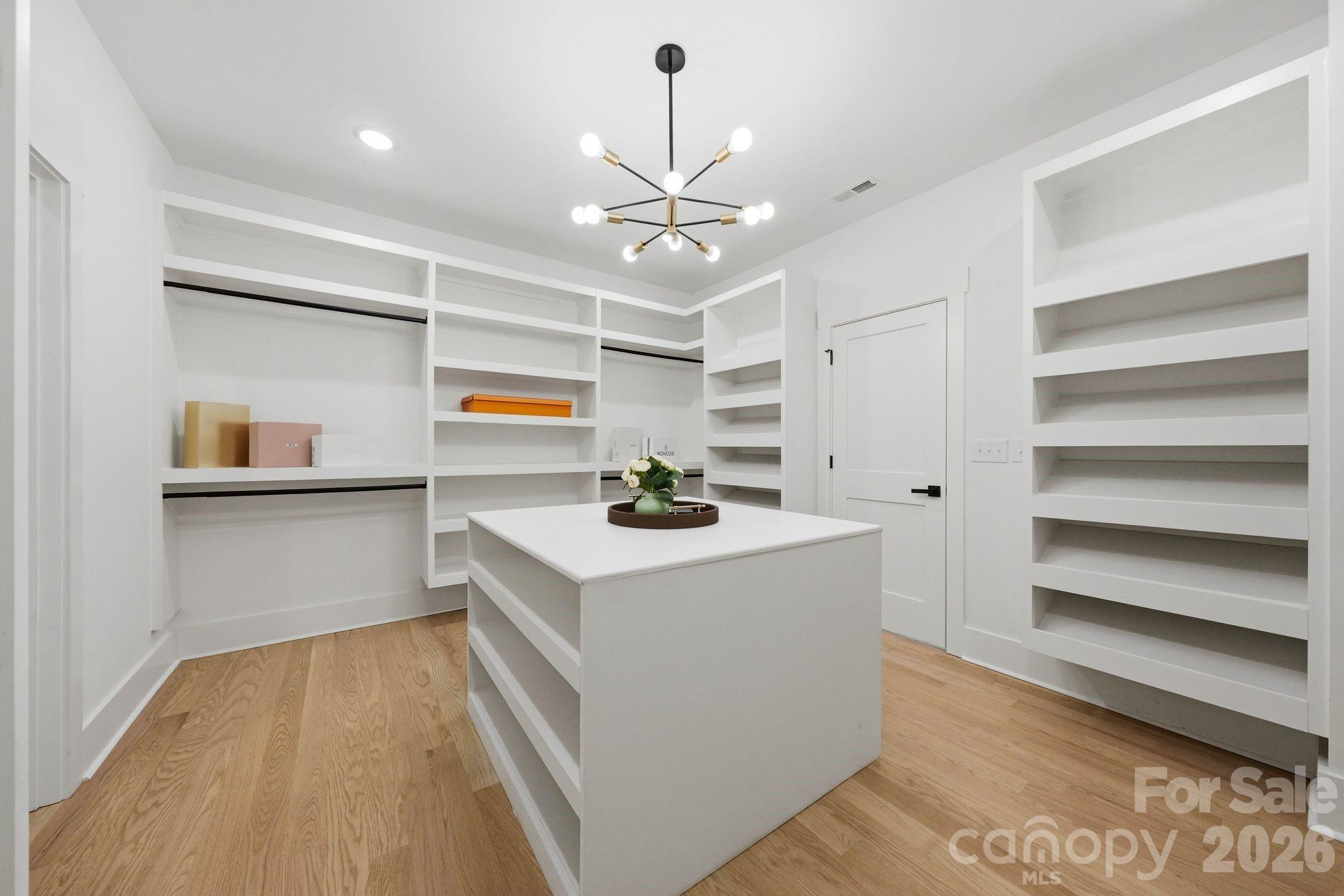 Walk-in closet with white built-in shelves, central island, light wood floors, and a modern chandelier.