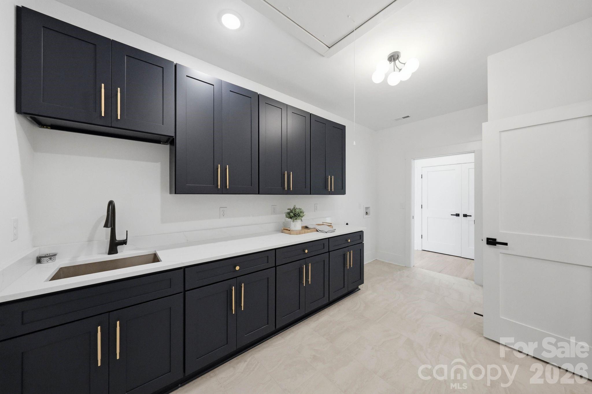 Laundry room with dark cabinets, brass hardware, and a long white counter with sink.
