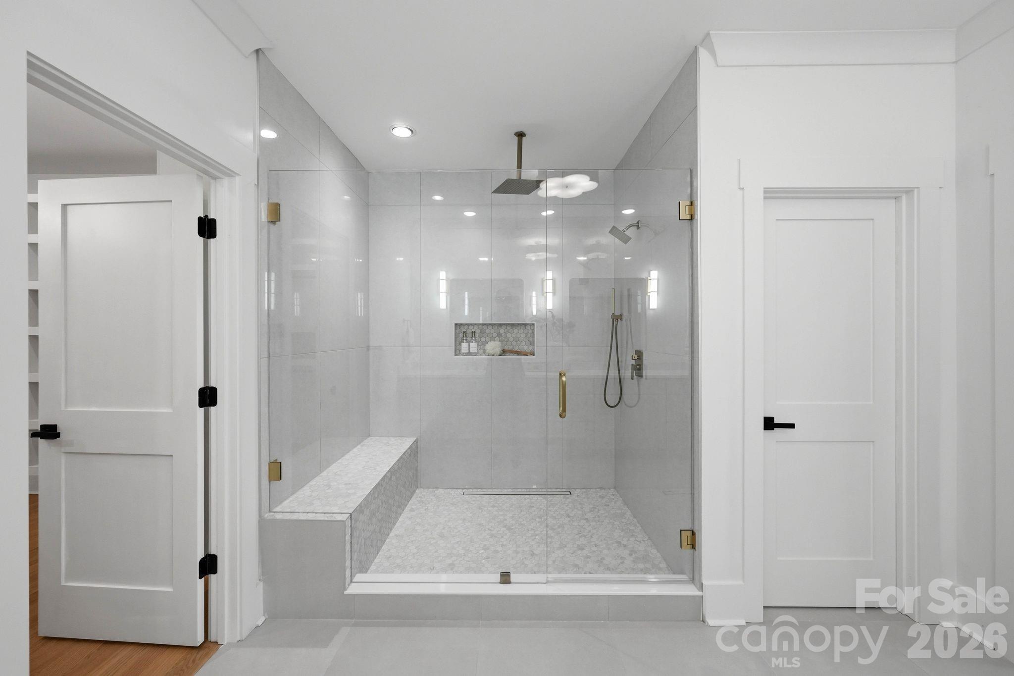 Modern bathroom with a glass walk-in shower, built-in bench, and brass hardware.