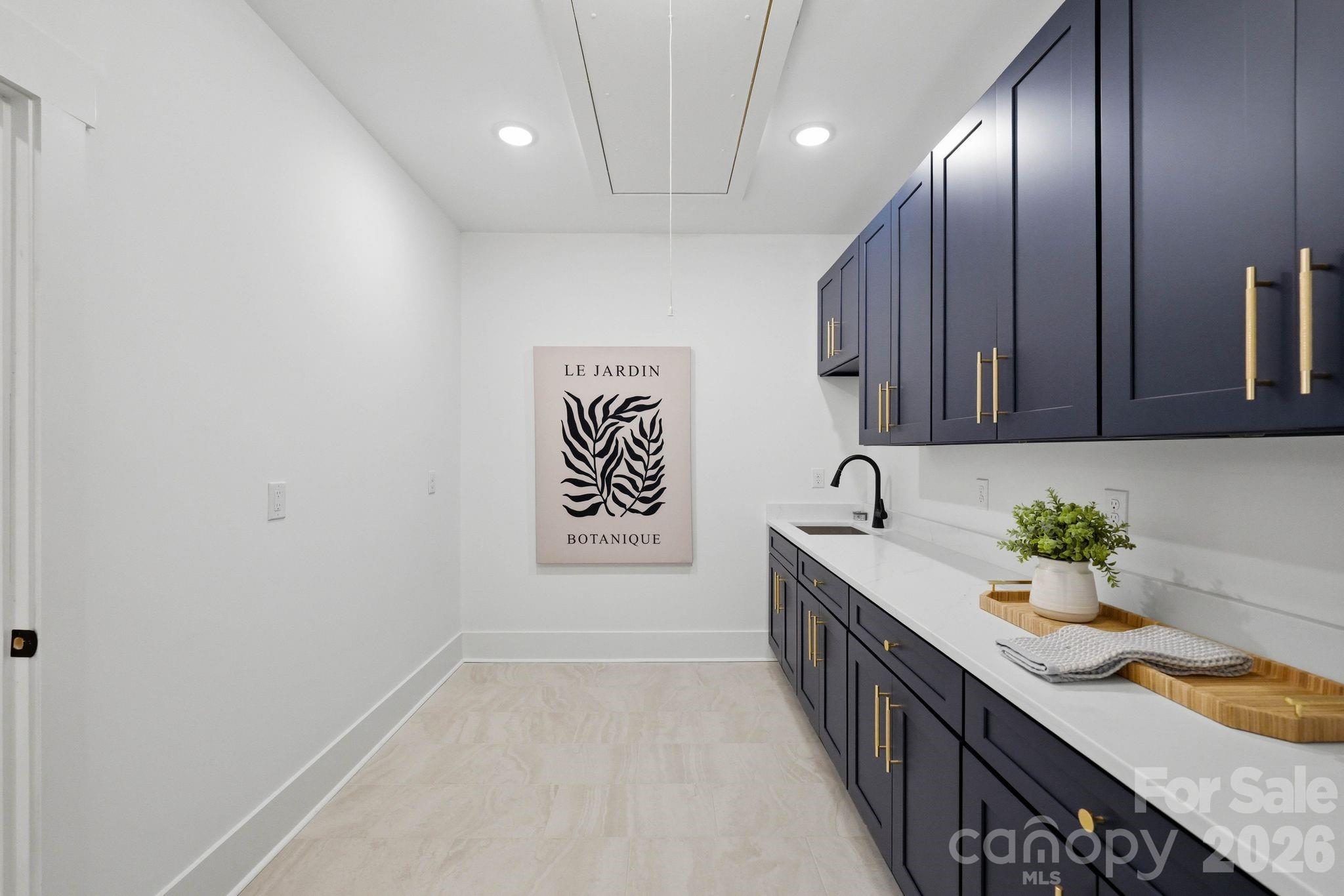 Laundry room with navy cabinets, brass pulls, a white counter, and a black faucet.