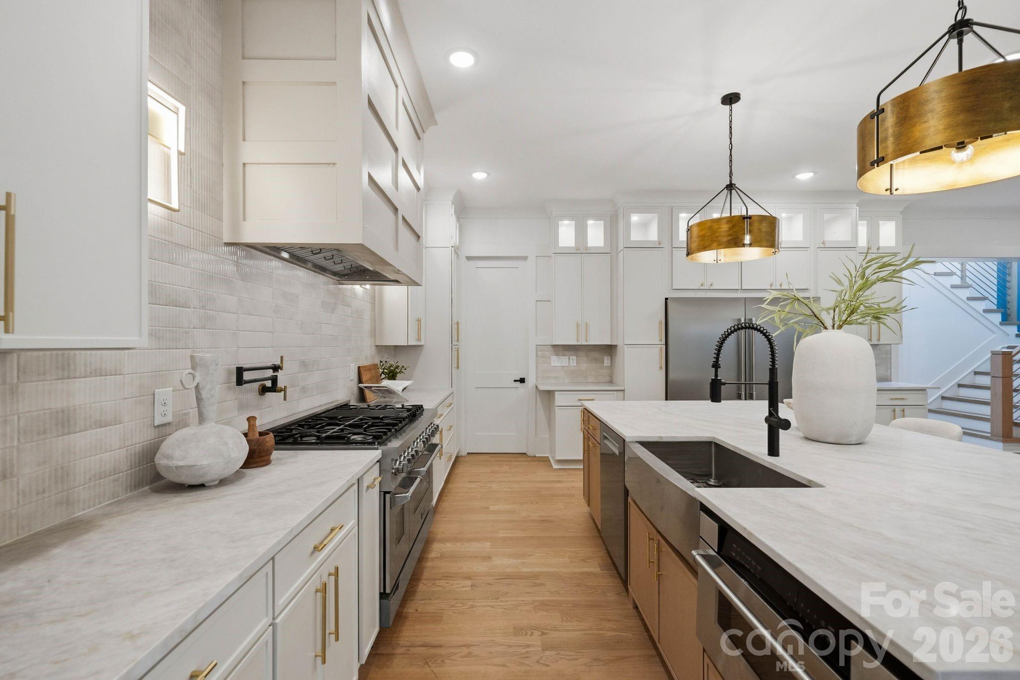 Bright kitchen with a large stone island, white cabinetry, brass pendants, and a stainless-steel range.