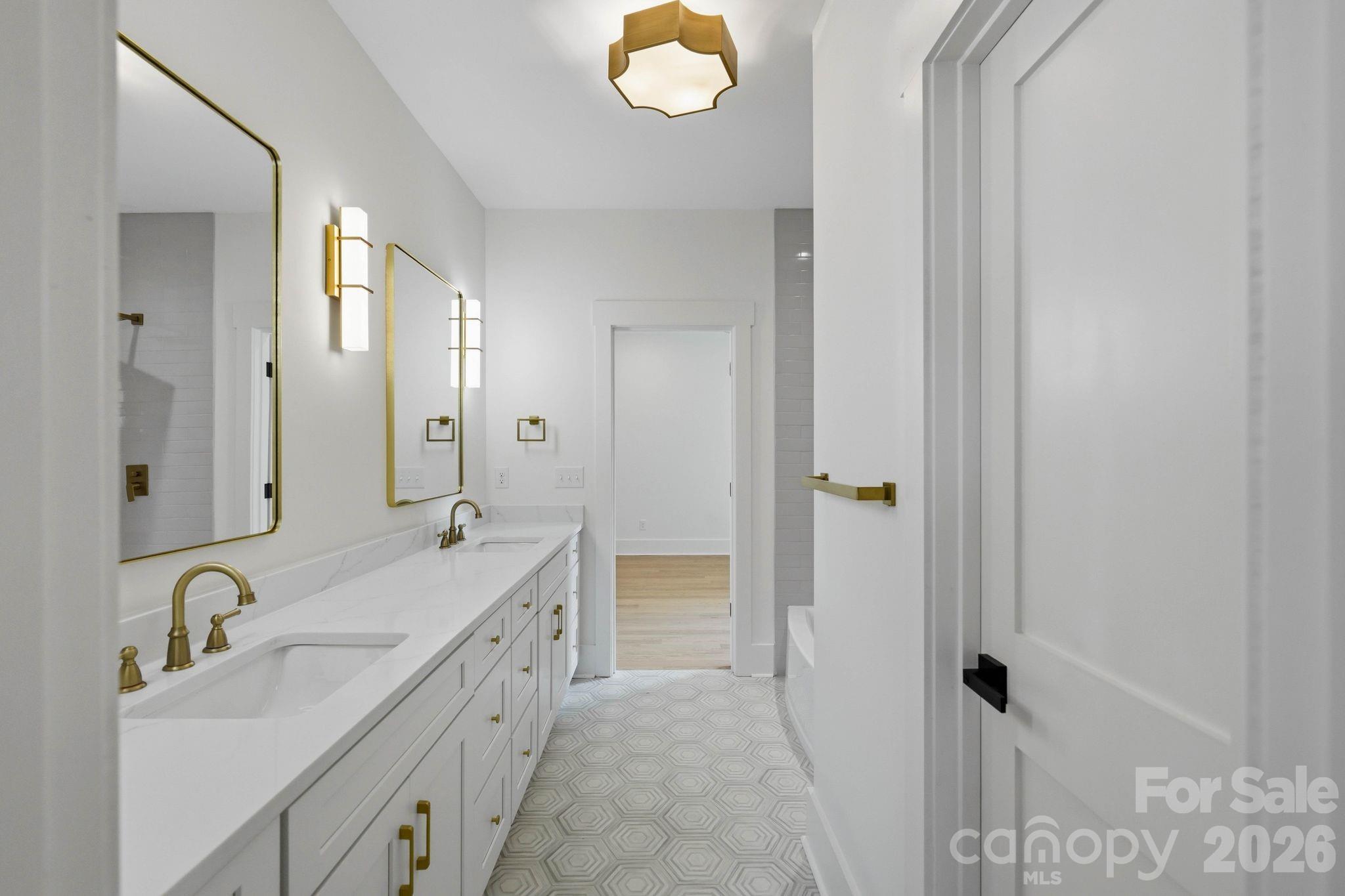 Renovated bathroom with a long white double vanity, brass fixtures, and geometric patterned floor tile.