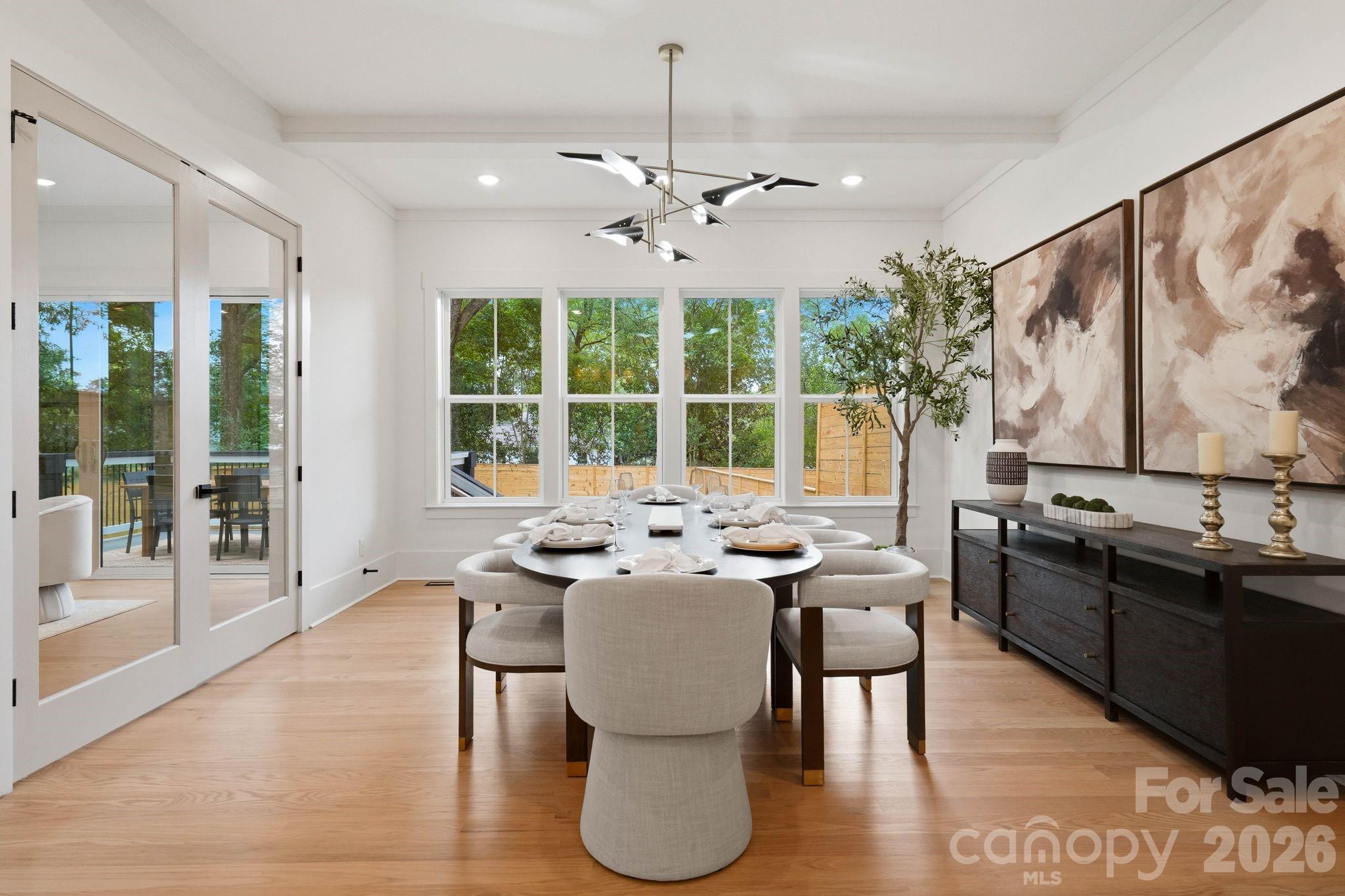 Staged dining room with a set table, large windows overlooking a deck, and light wood floors.