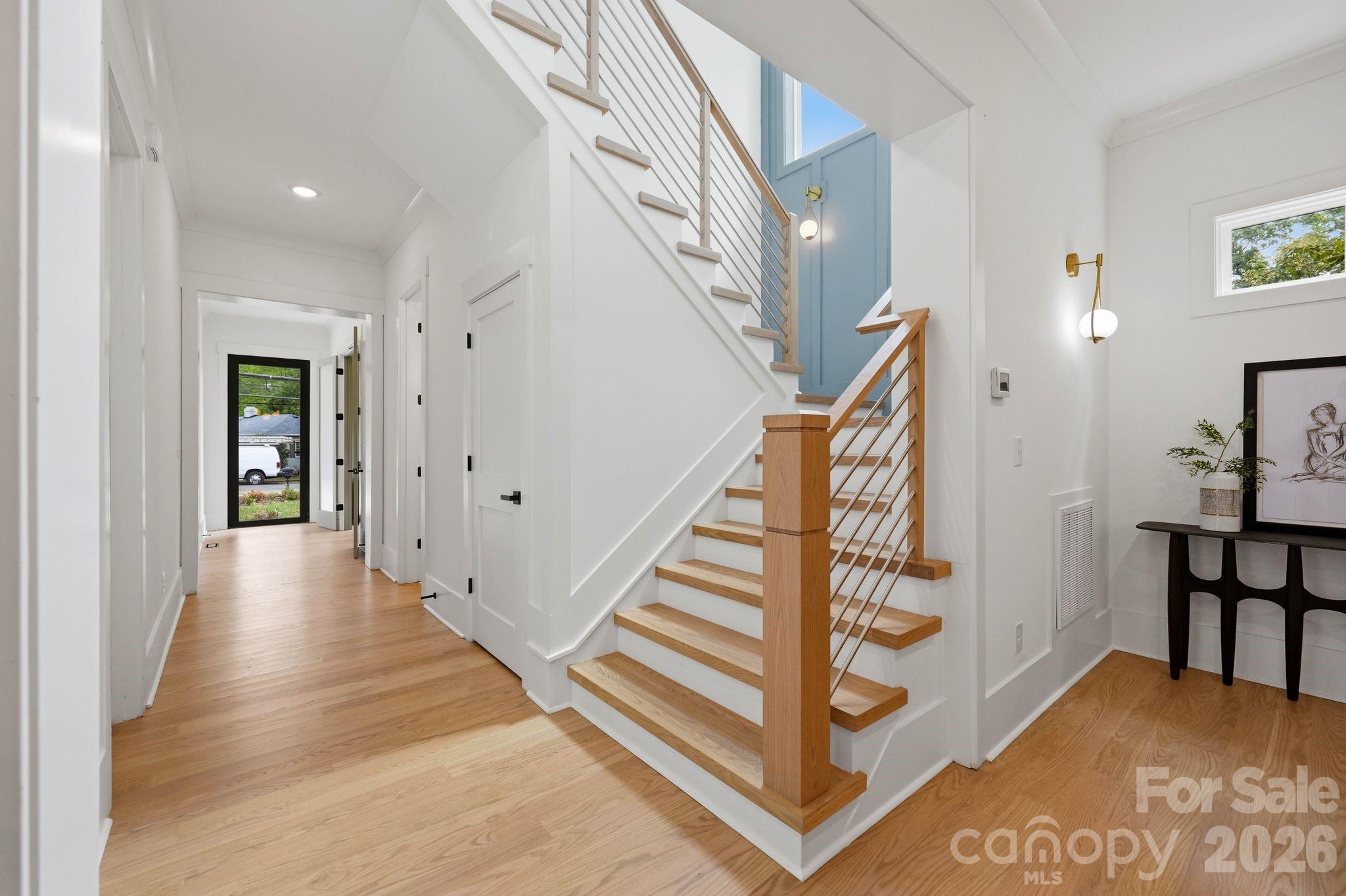 Bright foyer with a wood-and-metal staircase, blue accent wall, and light wood floors.
