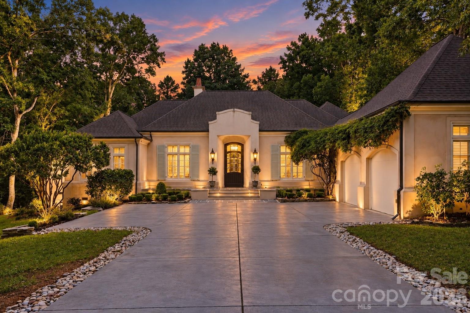 Luxury home with an illuminated entry, broad driveway, and landscaped grounds at dusk.