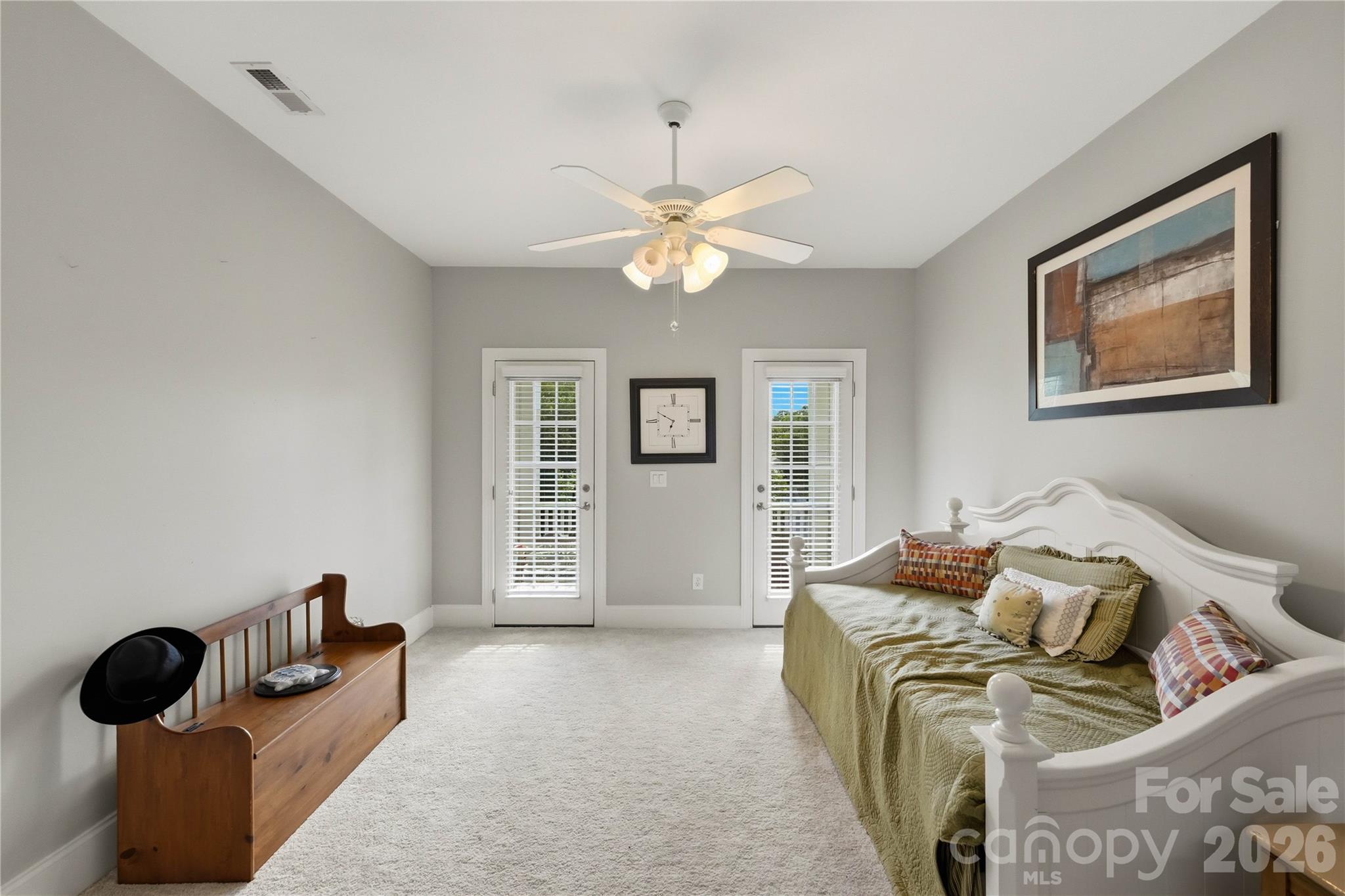 Furnished bedroom with a white daybed, green quilt, wooden bench, and two narrow doors with blinds.