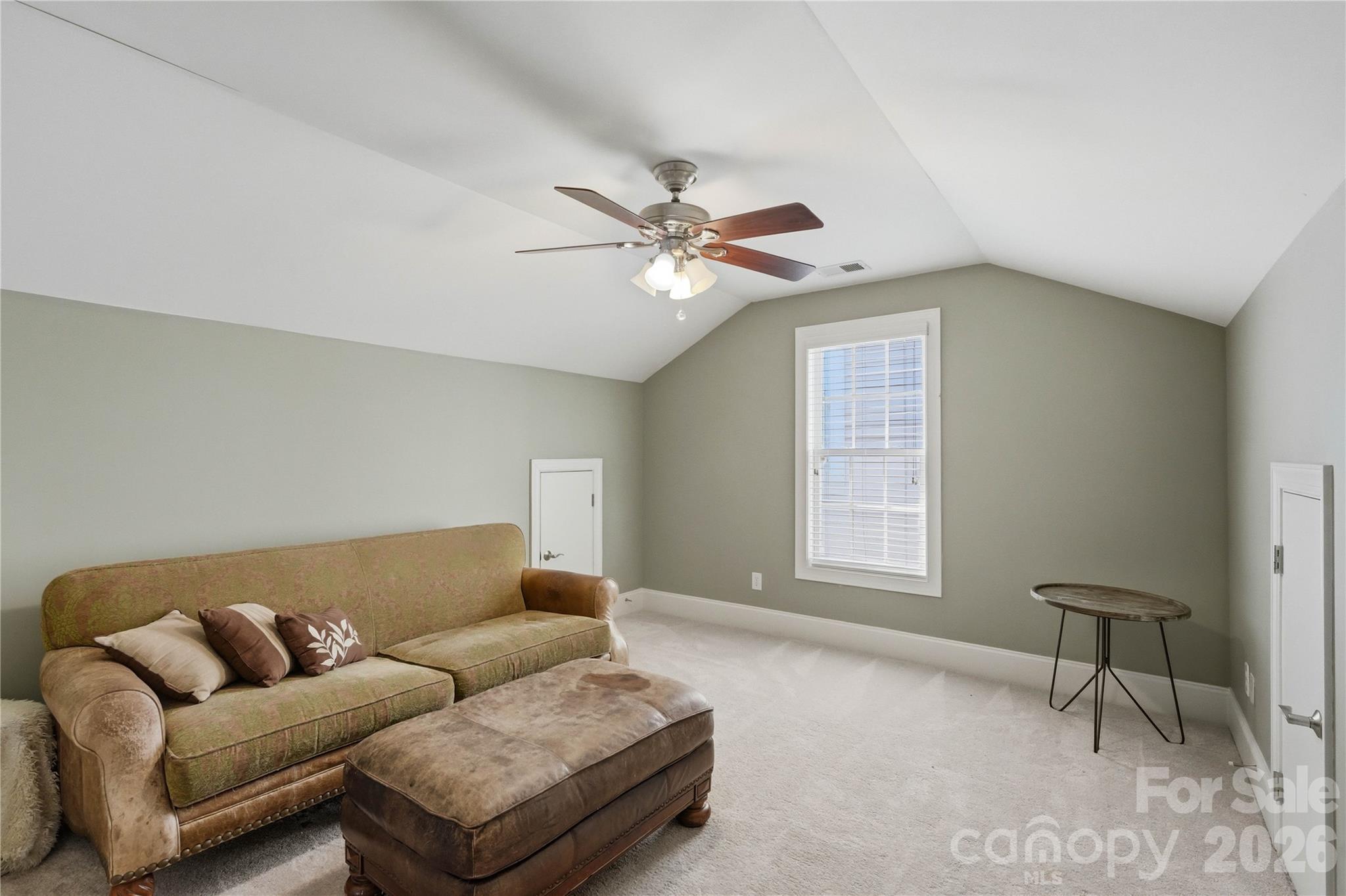 Furnished sitting room with a vaulted ceiling, ceiling fan, tan sofa, ottoman, and tall window.