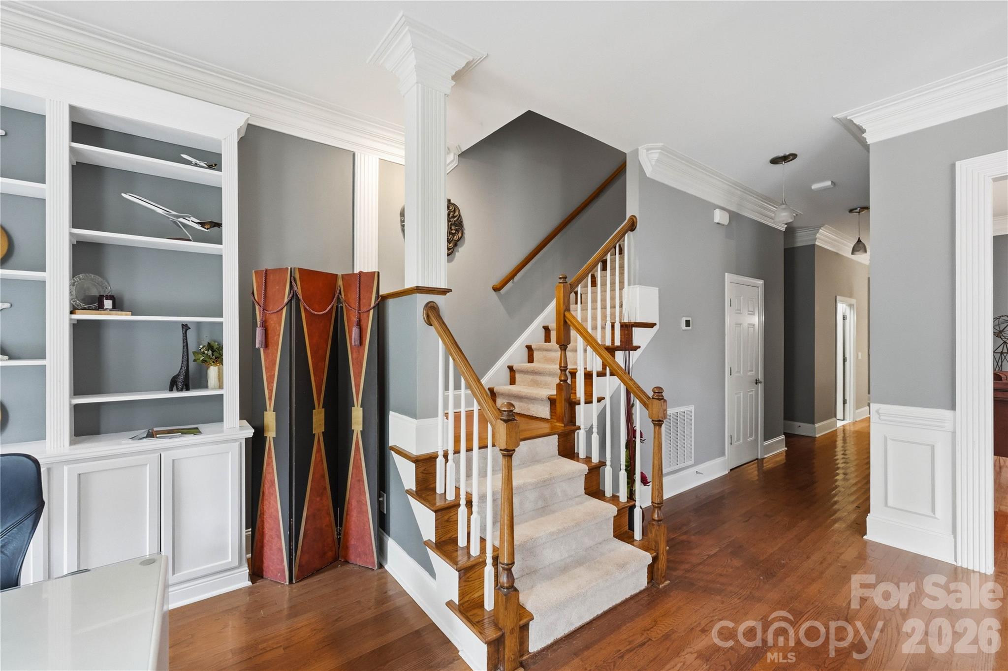 Foyer staircase with carpeted steps, polished wood railings, hardwood floors, and built-in display shelves.