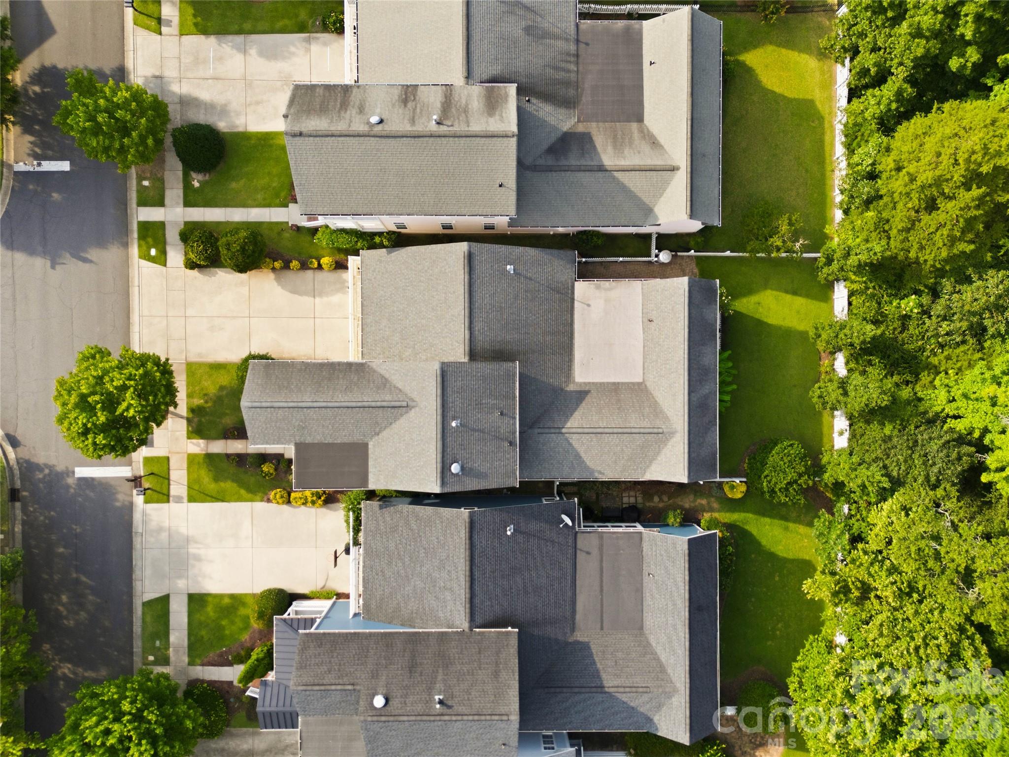Aerial view of neighboring homes with gray roofs, driveways, and tree-lined lawns.