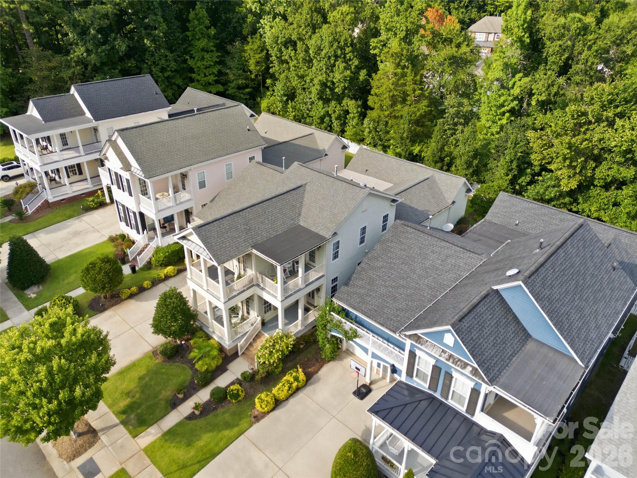 Aerial view of homes with covered porches, landscaped yards, and dense trees behind them.