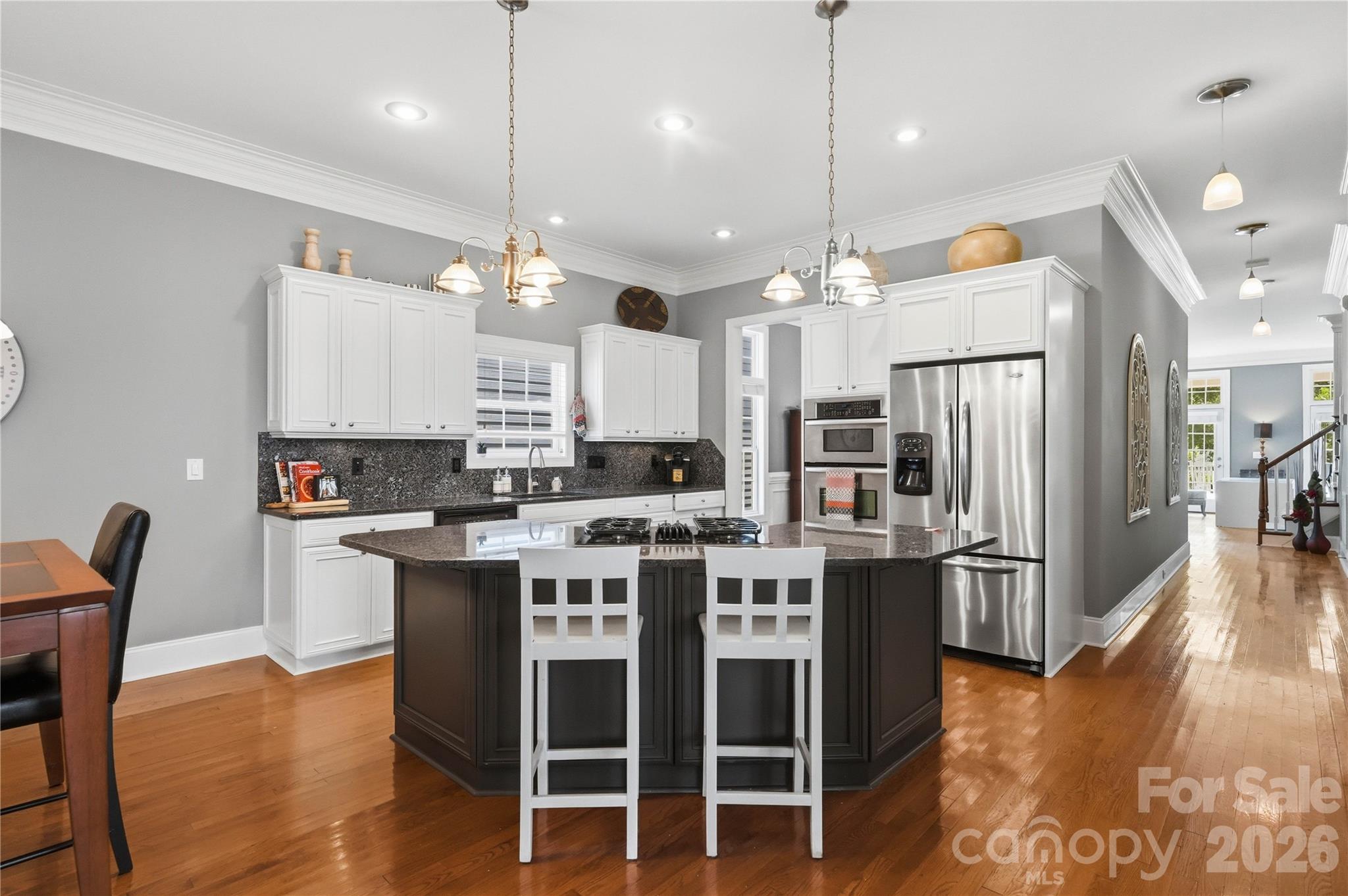 Kitchen with a large dark island, white cabinetry, stainless steel appliances, and hardwood floors.