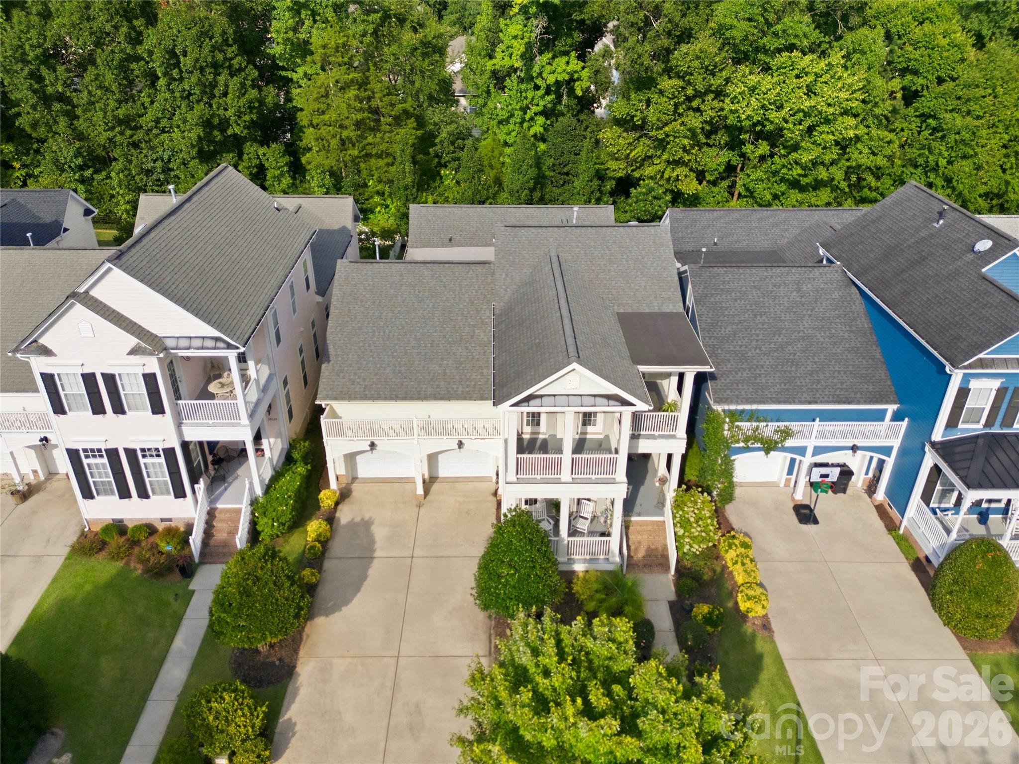 Aerial view of a two-story home with white porches, a wide driveway, and landscaped front yard.