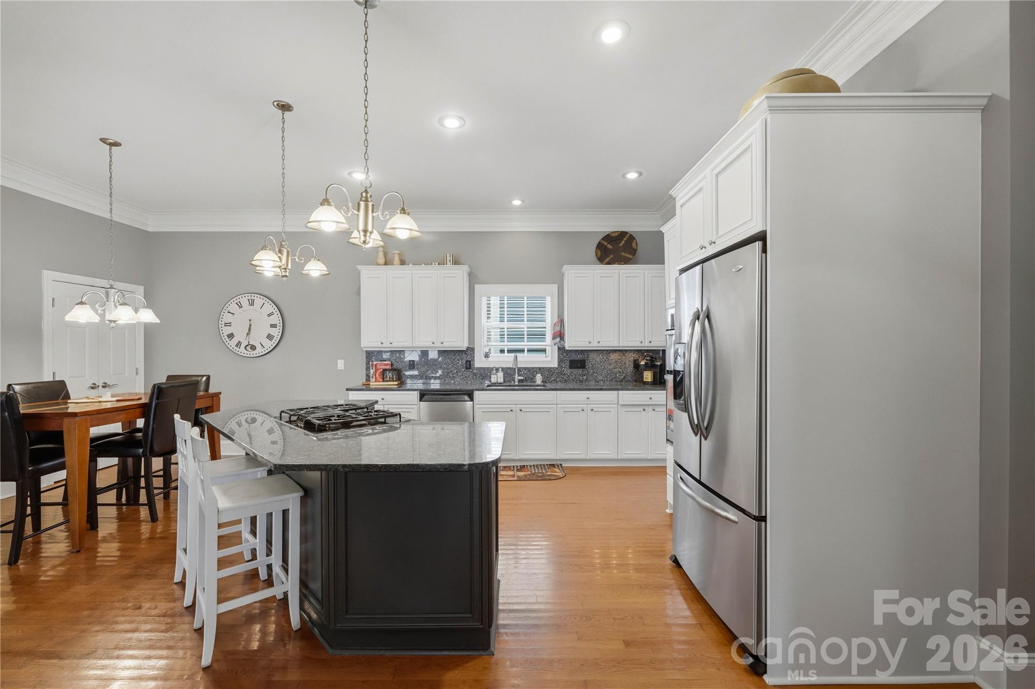 Kitchen with white cabinetry, stainless steel appliances, a dark cooktop island, and an adjoining dining table.