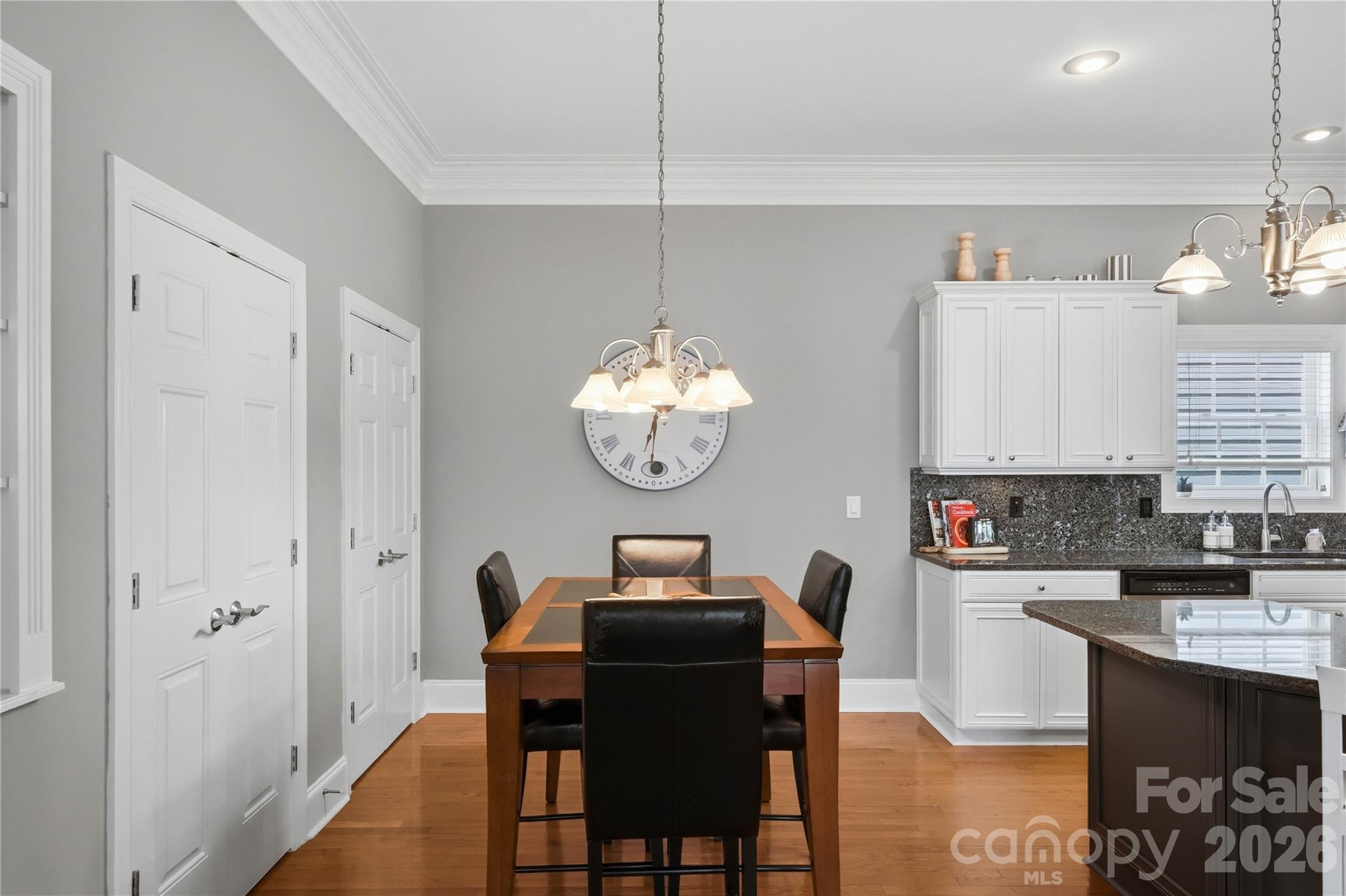 Dining area with a wood table beside a white-cabinet kitchen and granite counters.