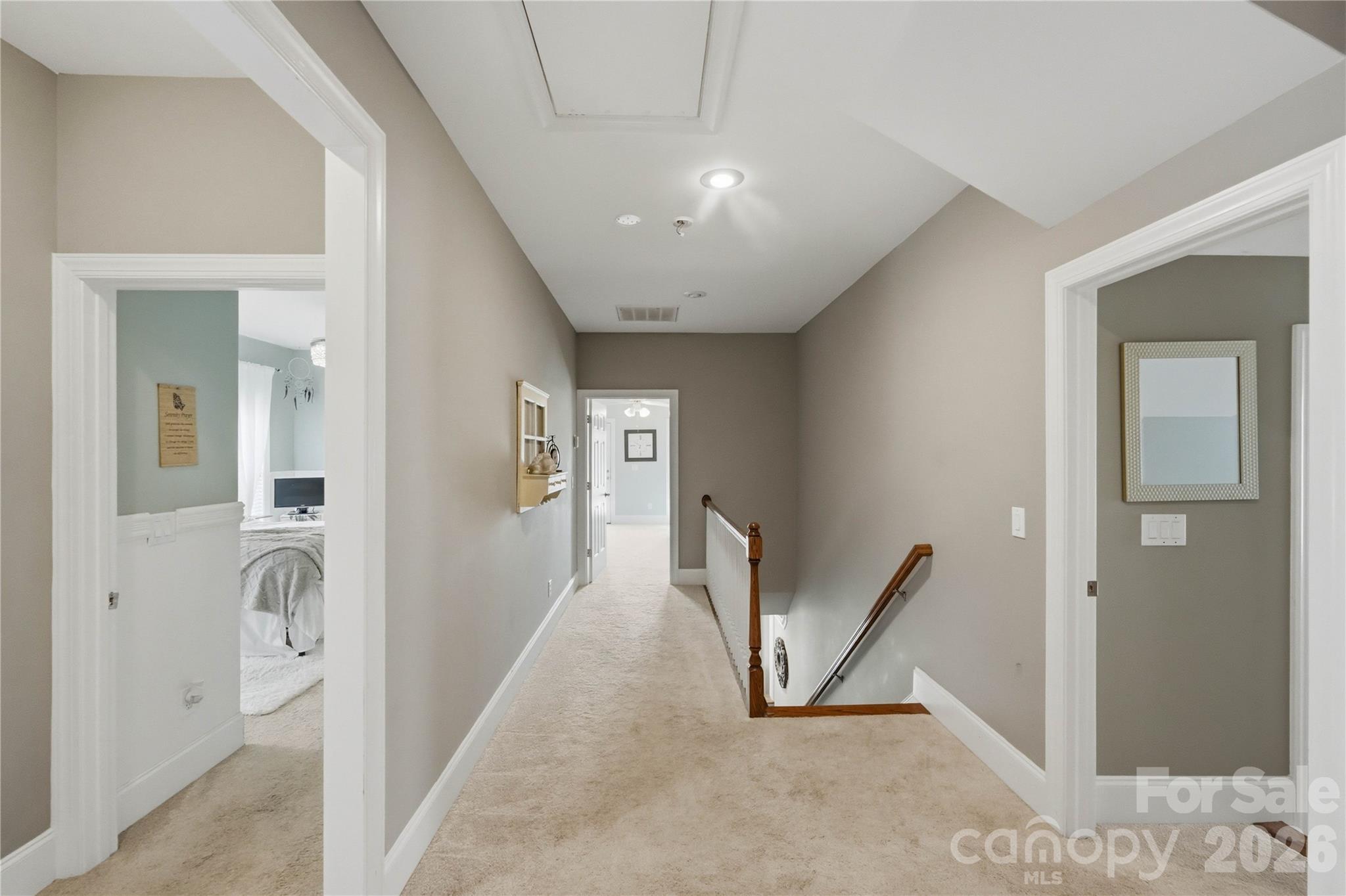 Upstairs hallway with beige carpet and a wooden stair railing between bedroom doorways.