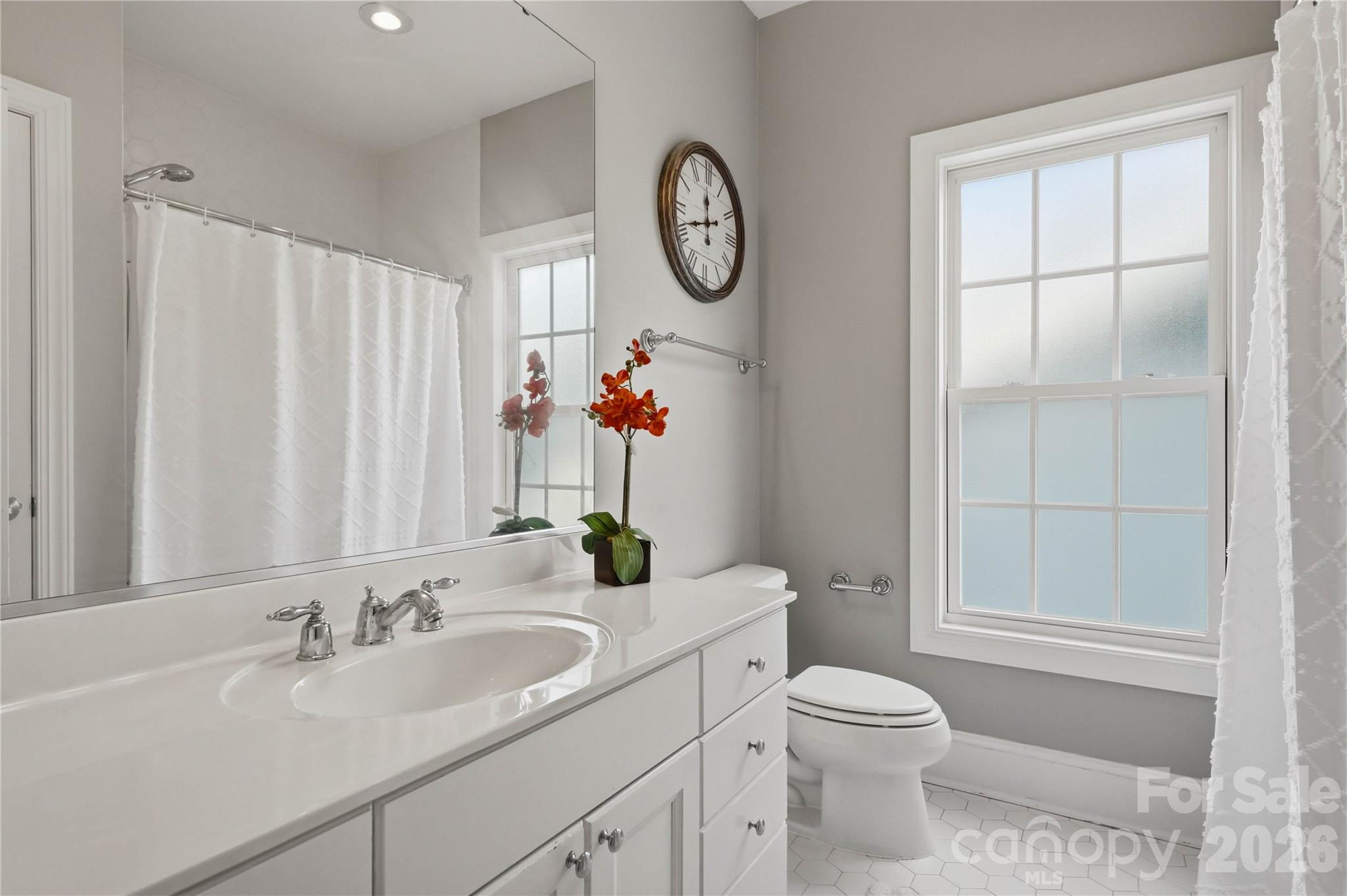 Bathroom with white vanity, frosted window, and orange orchid beside a round wall clock.
