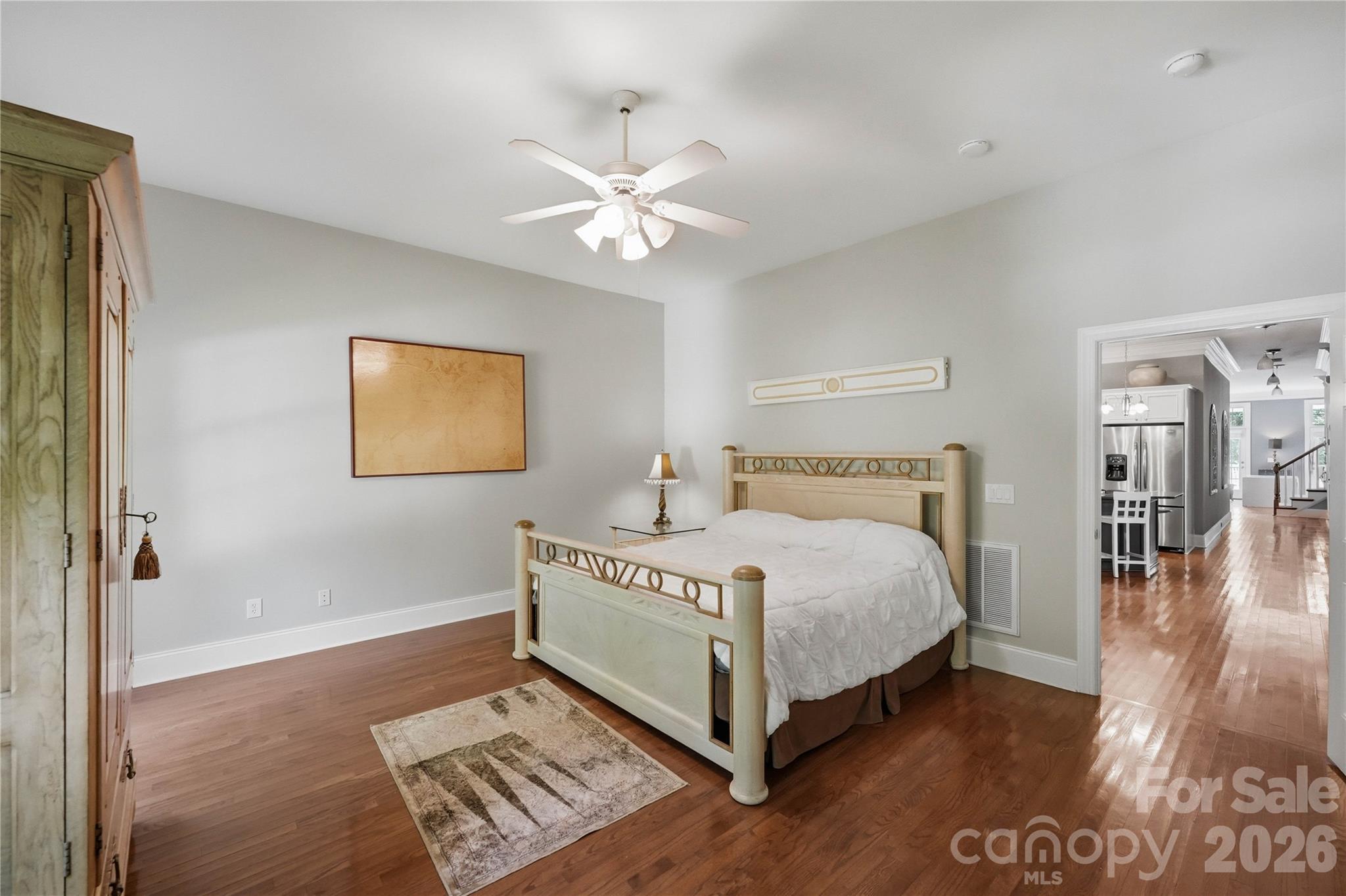 Bedroom with a pale wood four-poster bed and hardwood floors, opening onto the kitchen and hallway.