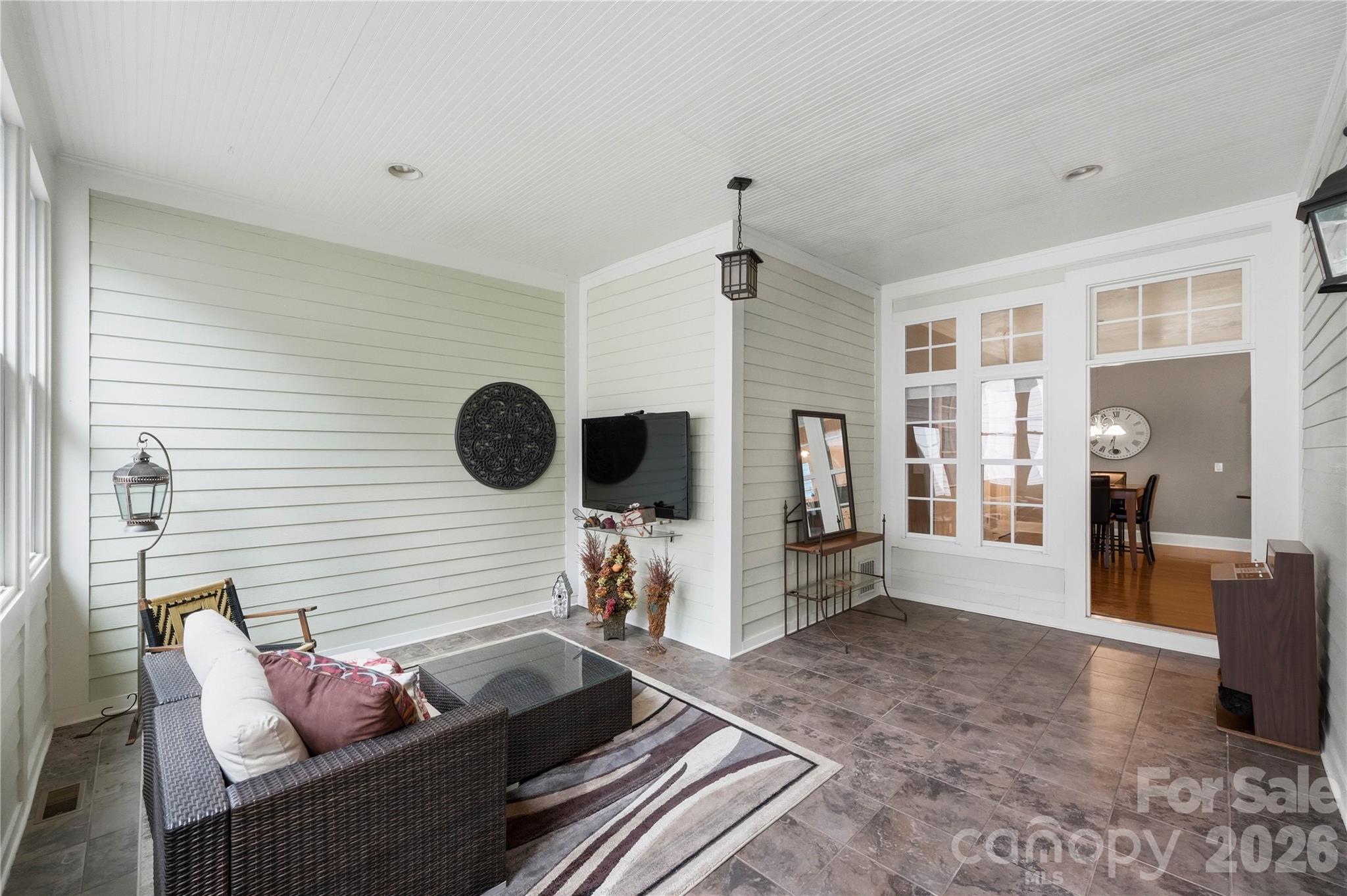 Furnished sunroom with a wicker sofa, tiled floor, and French doors opening to a dining area.