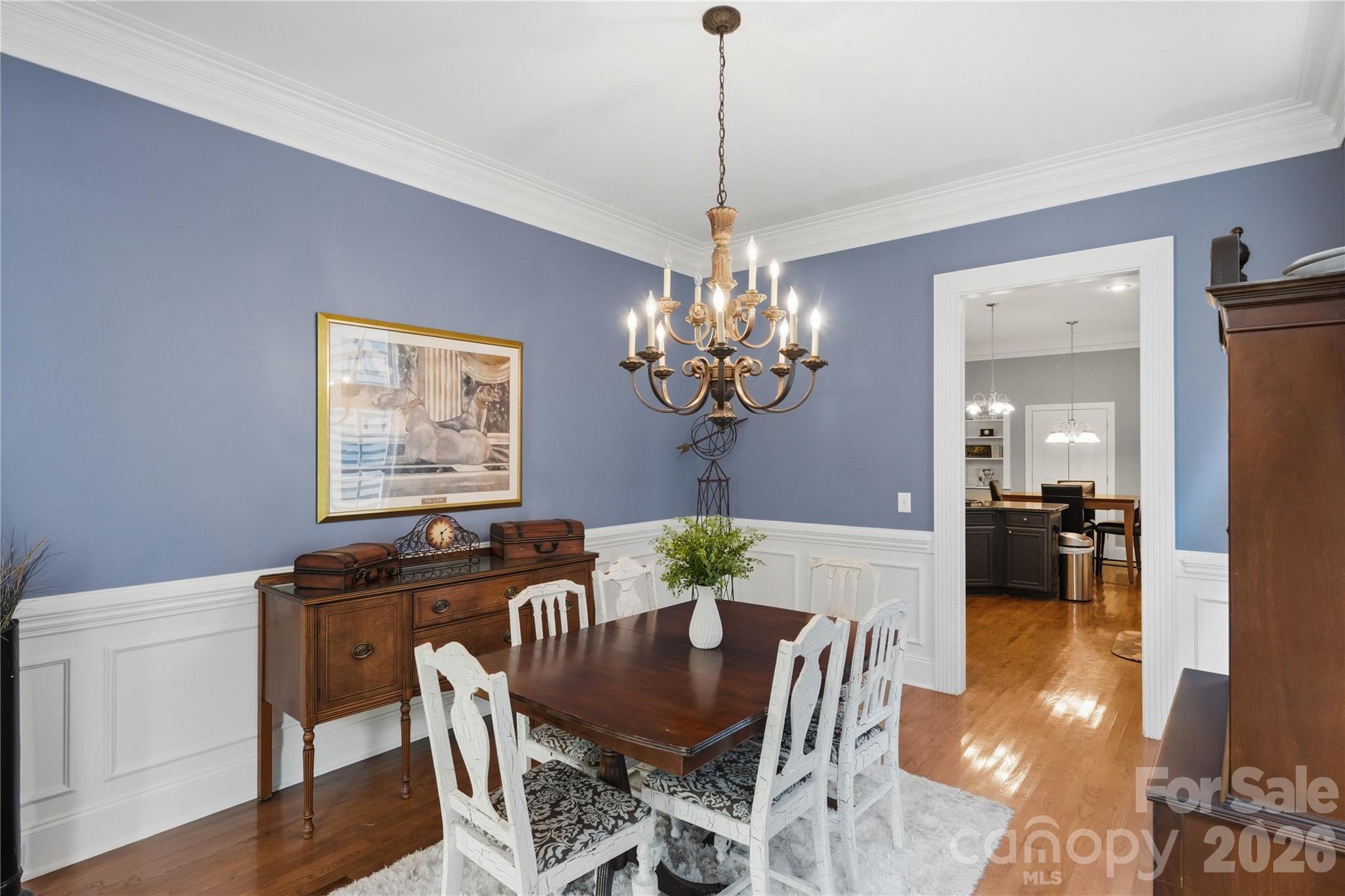 Dining room with blue walls, white wainscoting, and a dark wood table beneath an ornate chandelier.
