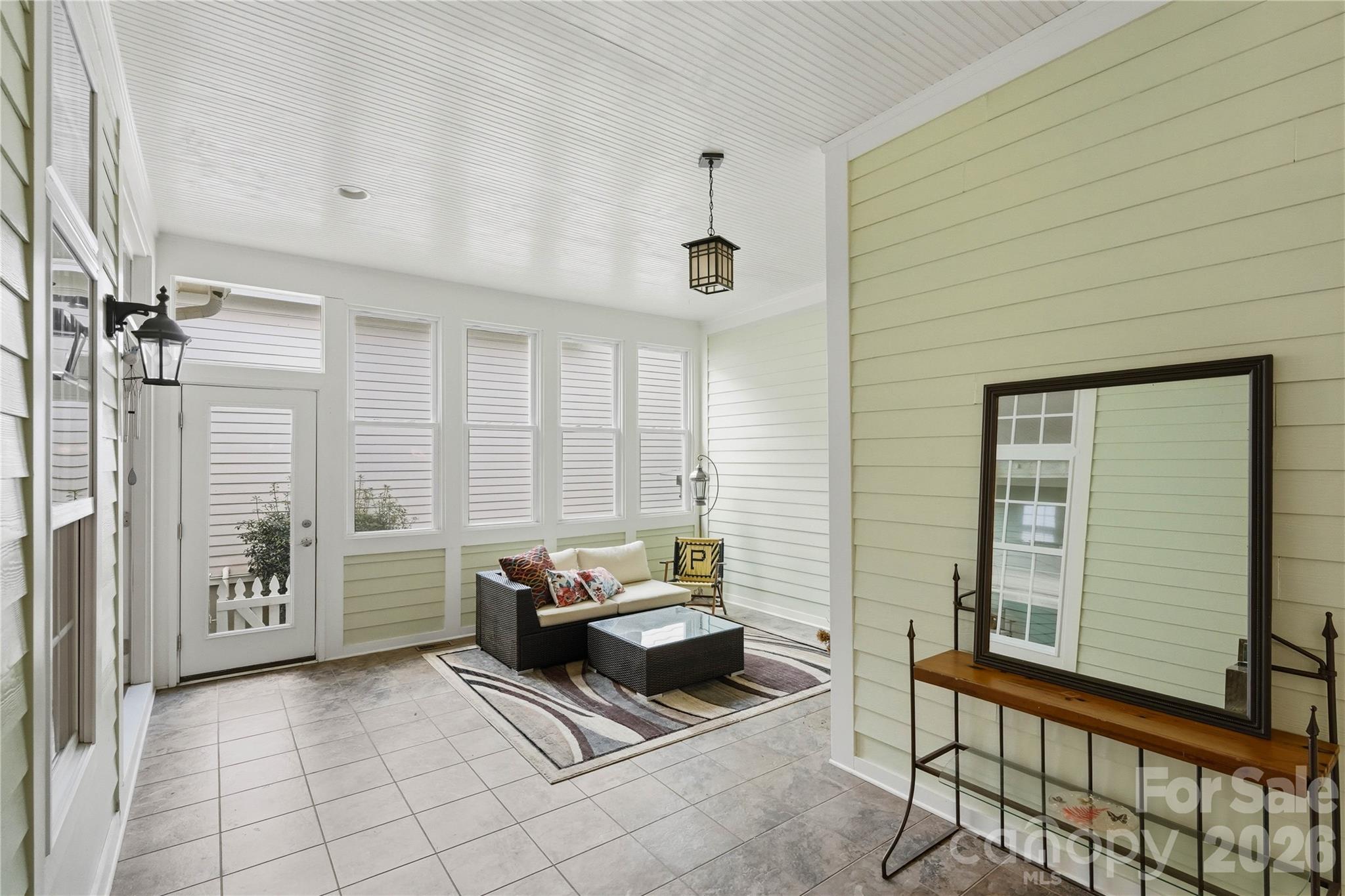 Enclosed sunroom with tall windows, tiled floor, and wicker seating beneath a white beadboard ceiling.